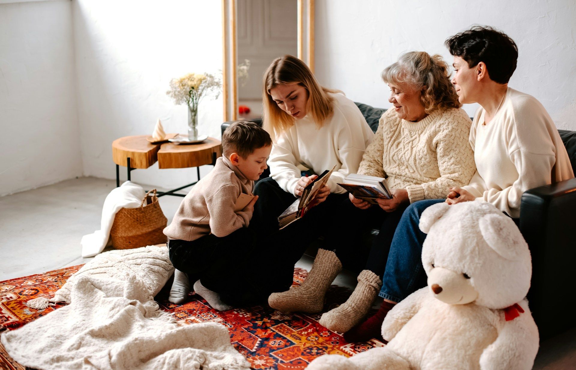Family sitting on a rug, opening a gift in a bright living room with a large white teddy bear nearby