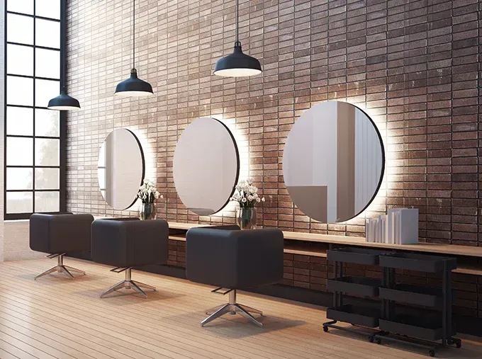 Modern salon interior with brick wall, round mirrors, black styling chairs, and pendant lights