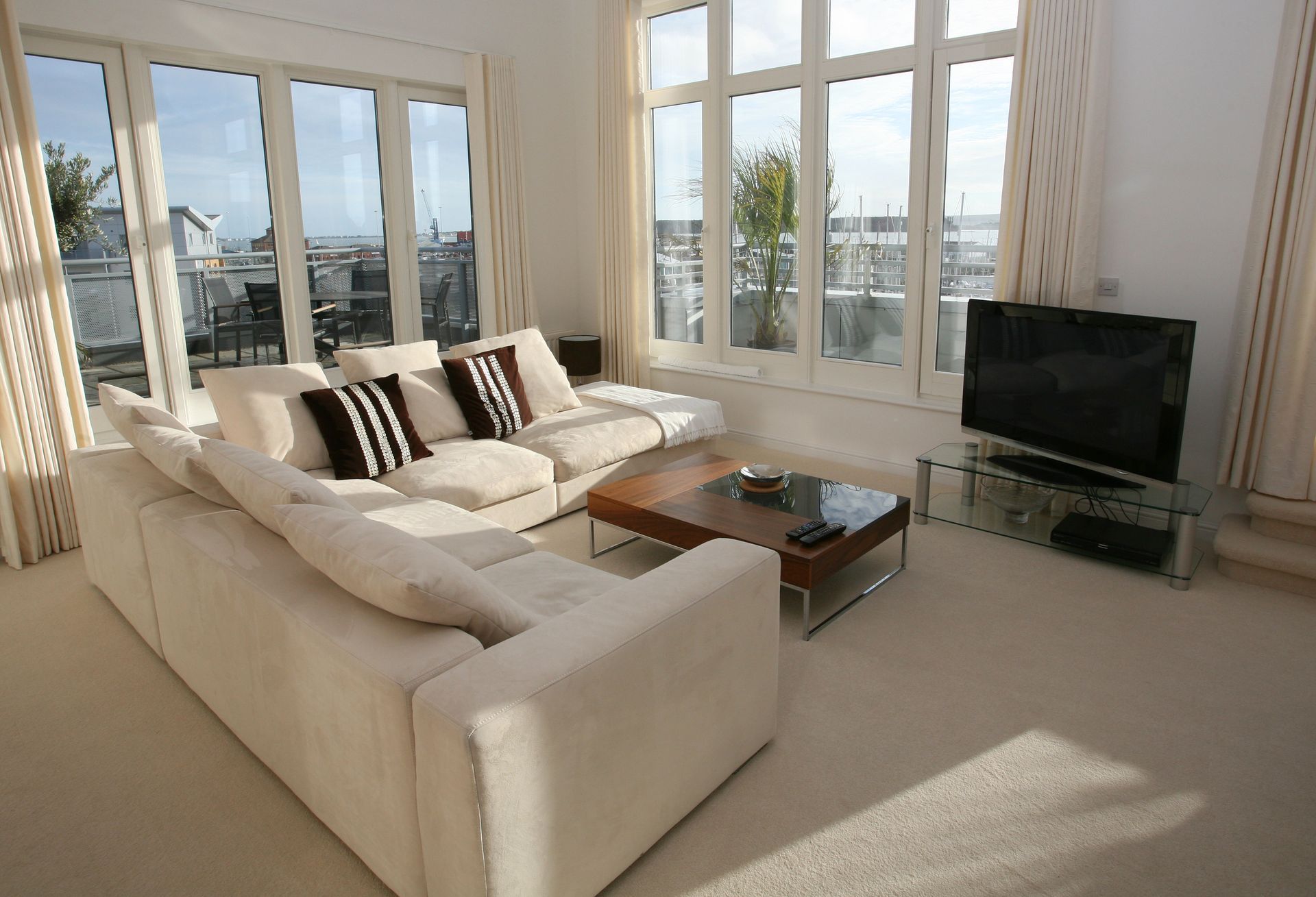 Bright modern living room with cream sofas, coffee table, TV, and large windows overlooking a sunny view