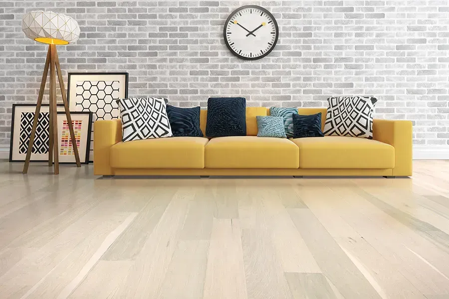 Modern living room with mustard sofa, patterned pillows, wall clock, and wooden floor against brick wall