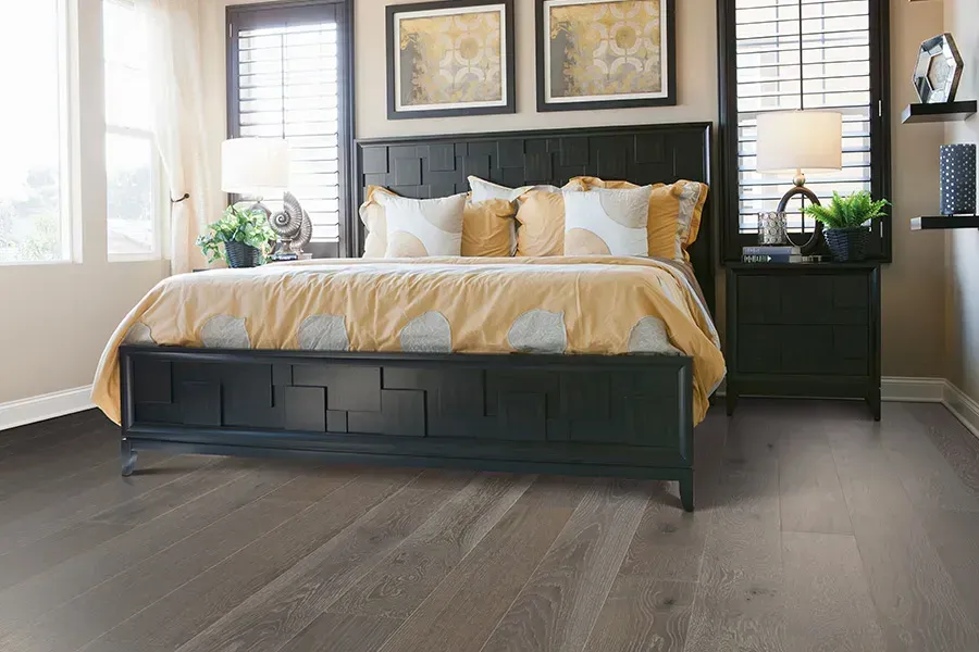Modern bedroom with a black bed, yellow bedding, nightstands, and windows with blinds