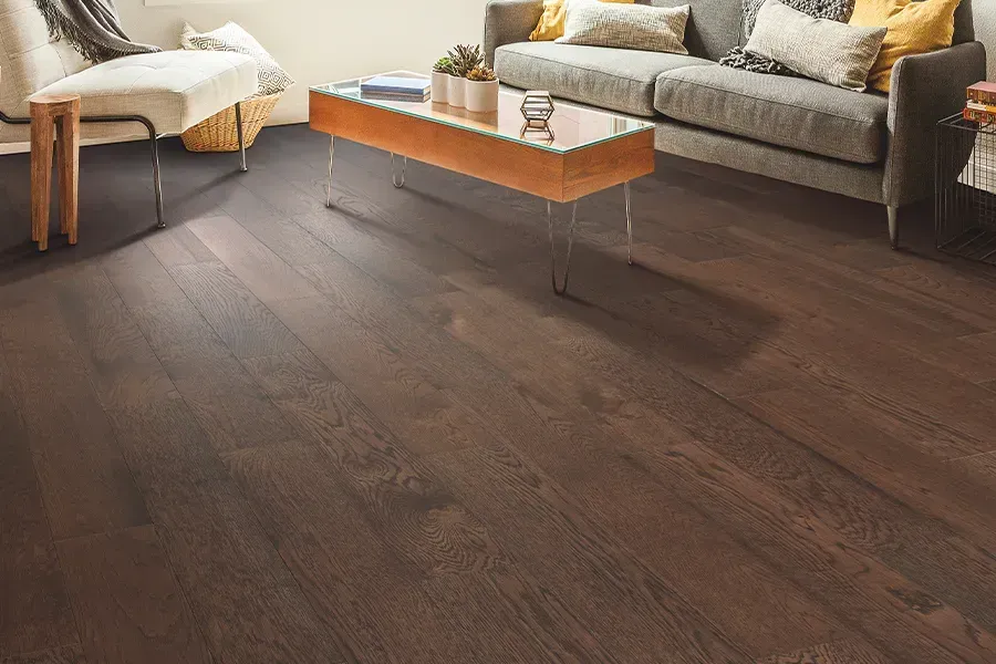 Modern living room with dark wood floor, gray sofa, ottoman, and wooden coffee table