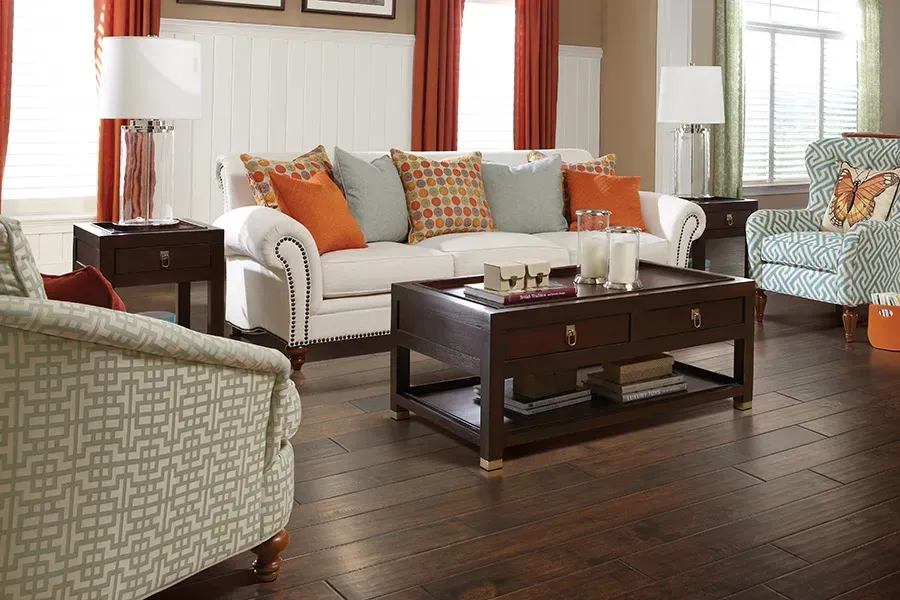 Cozy living room with white sofas, orange accents, a dark wood coffee table, and hardwood floors