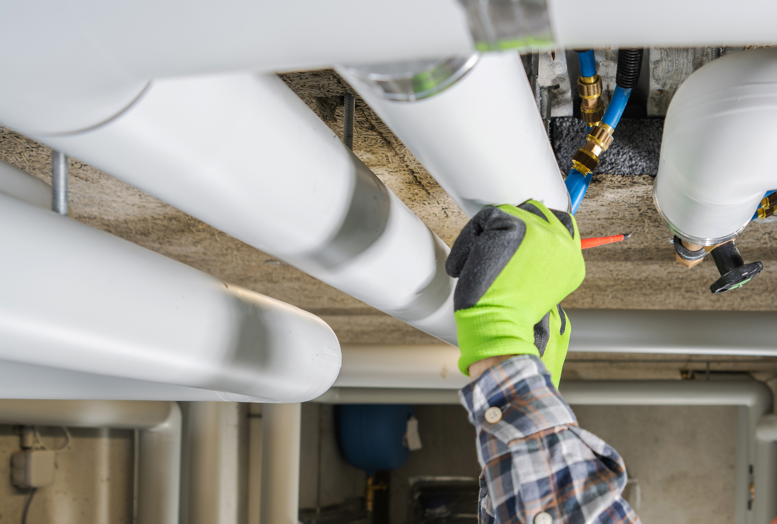 Gloved hand inspecting insulated pipes and valves under a ceiling in a utility room