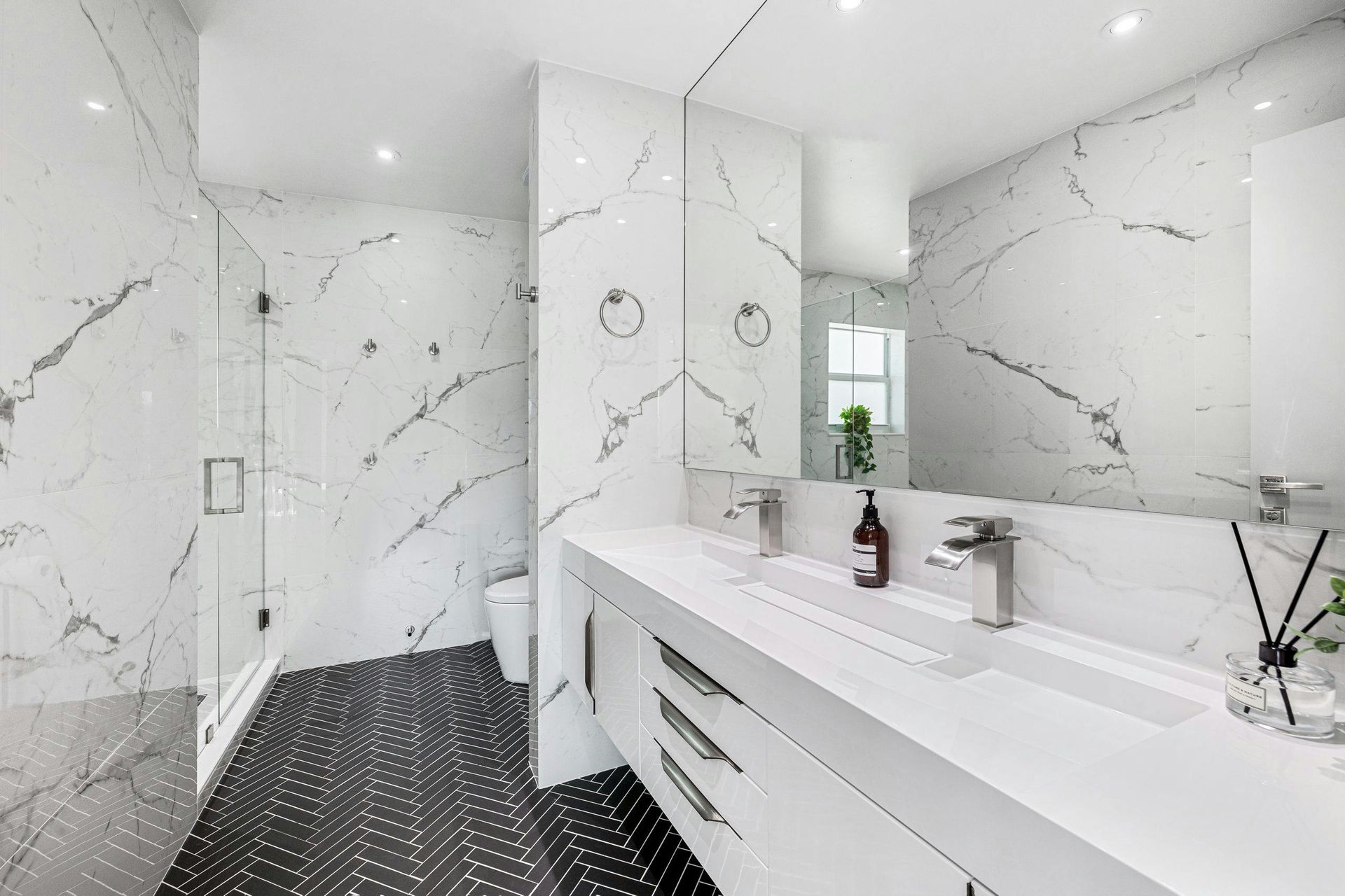 Modern white bathroom with marble-look walls, black hex tile floor, and a long double vanity sink.