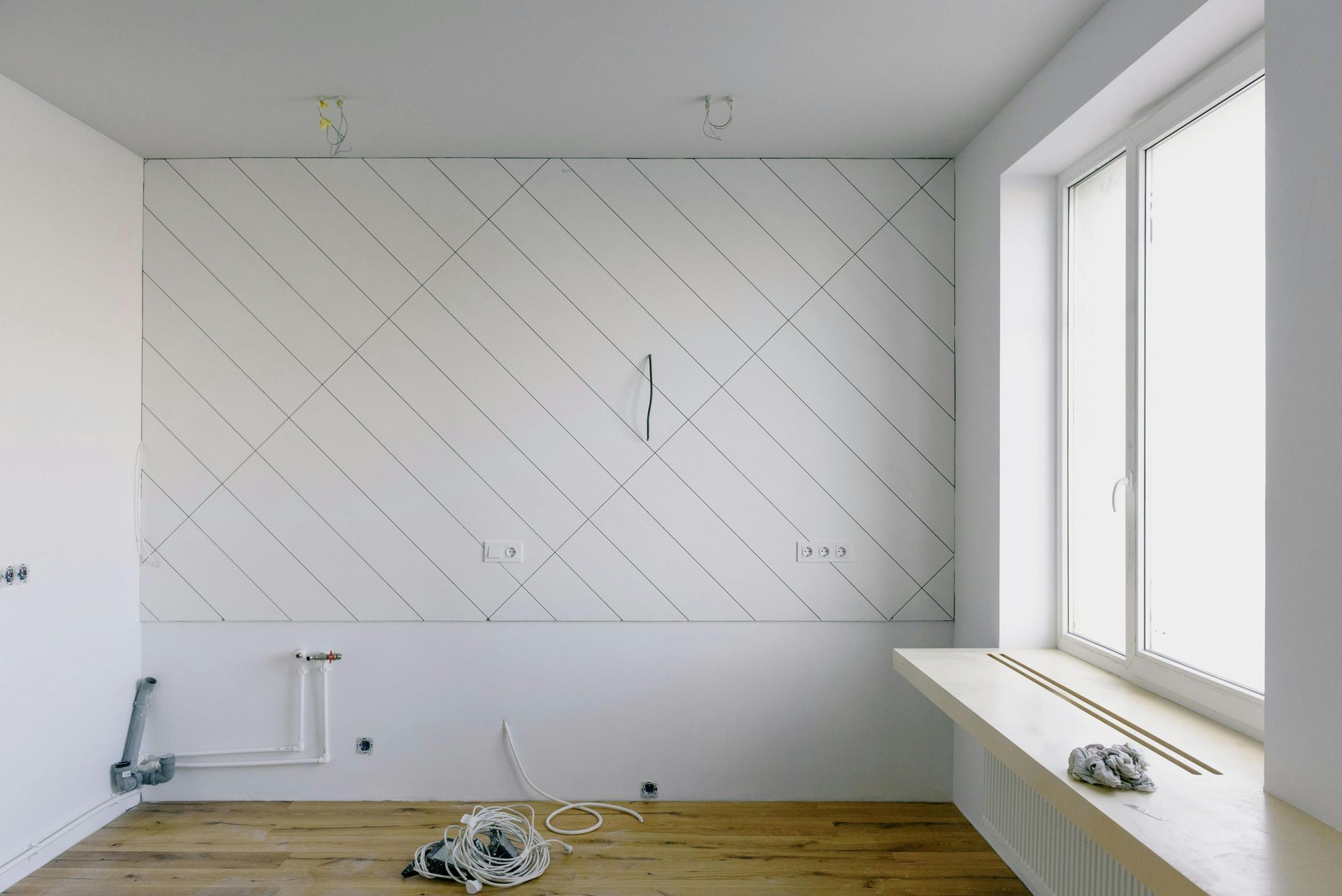 Empty white room with diagonal wall markings, wood floor, and large window light on the right.