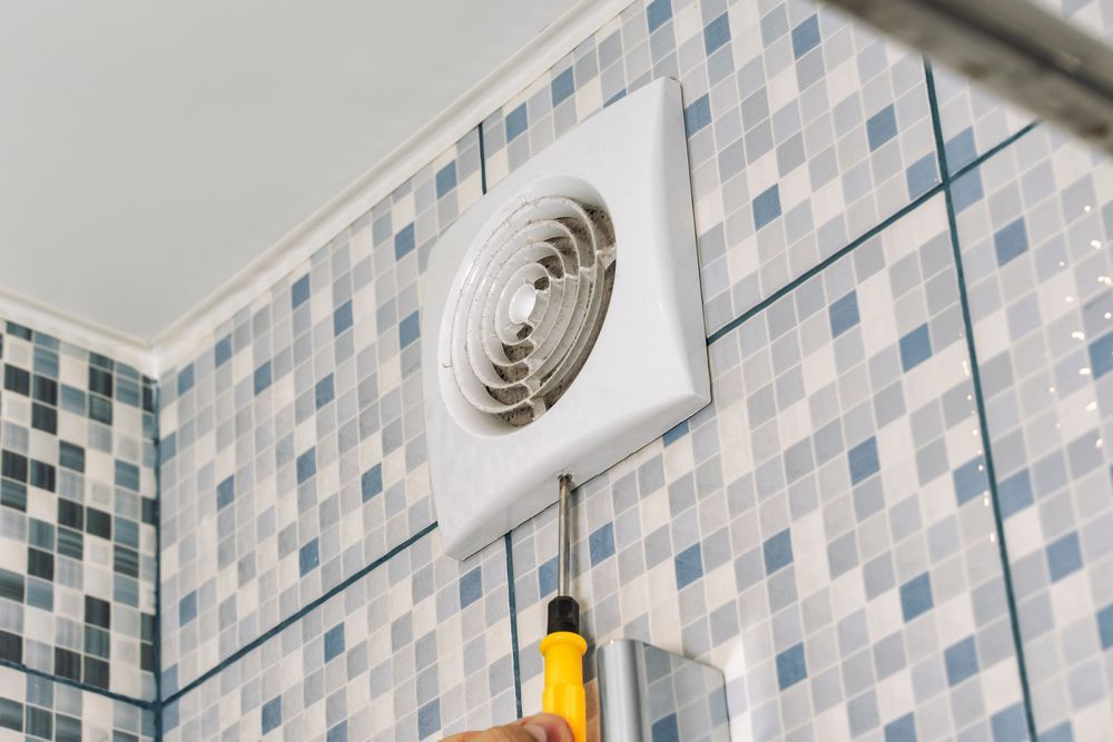 A Person is Installing a Bathroom Fan on a Tiled Wall — Comfort Solutions in Kunda Park, QLD