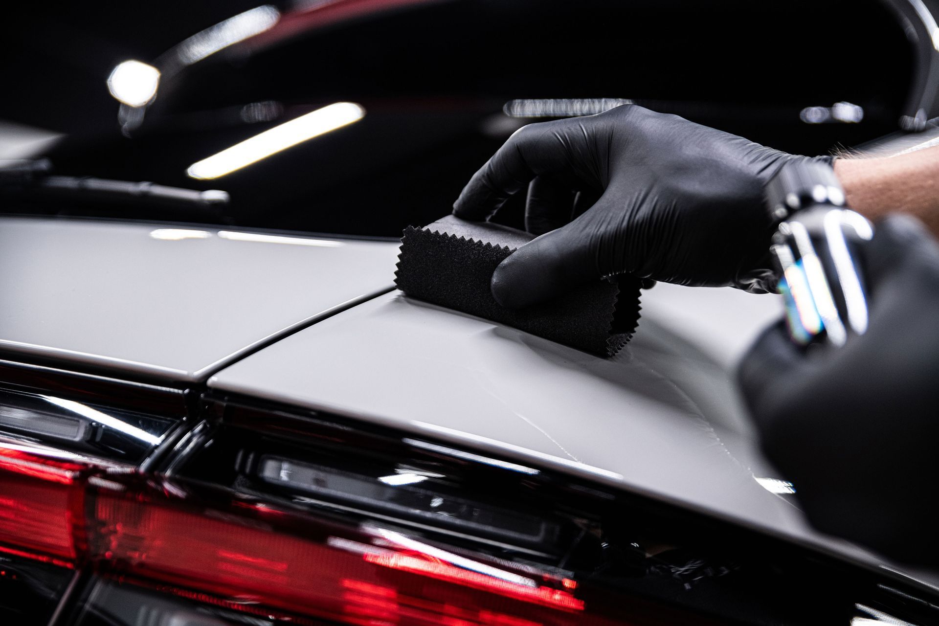 A person wearing black gloves is polishing a car with a sponge.
