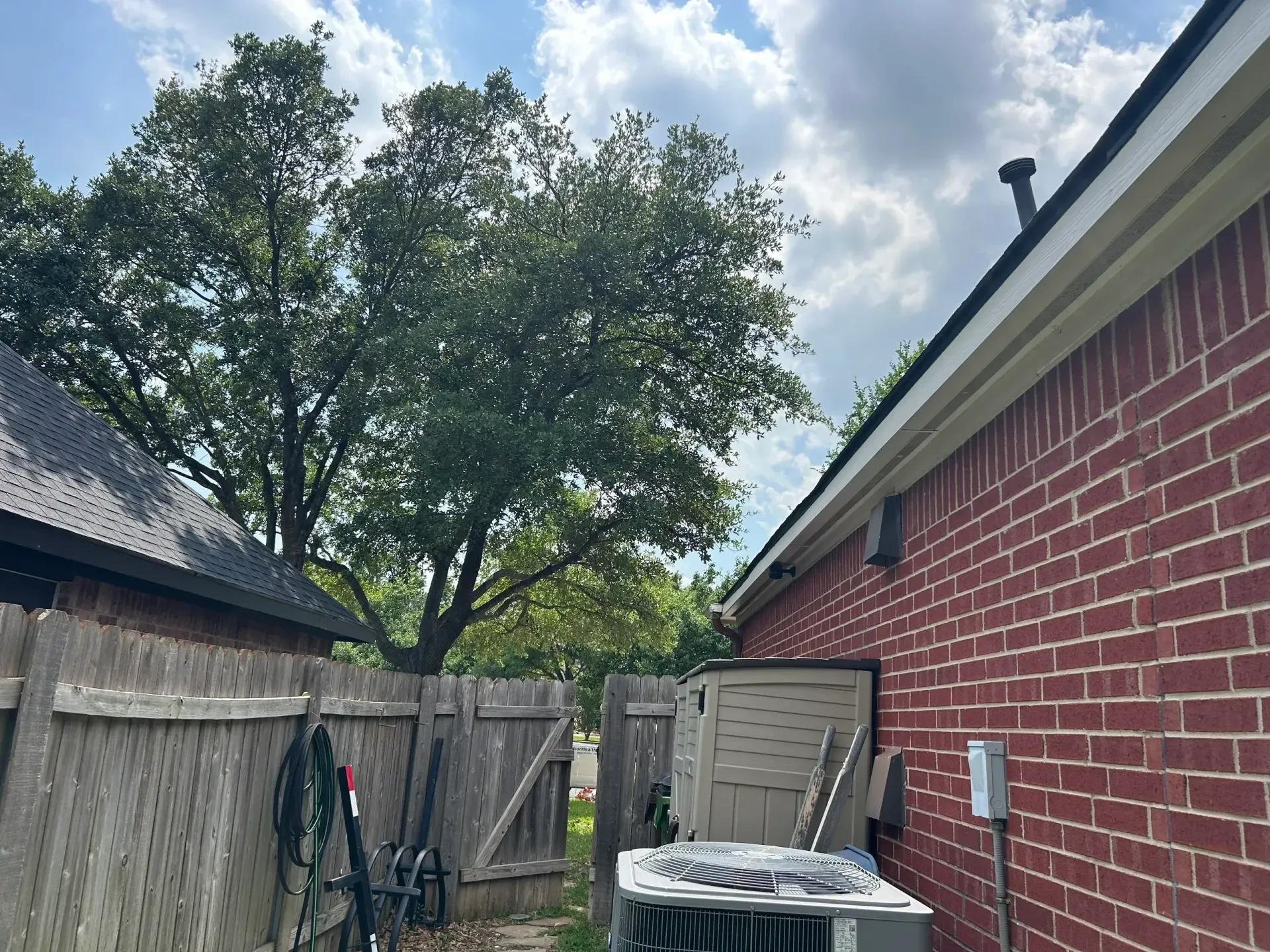 Brick building, wooden fence, tree, air conditioning unit under a cloudy sky.