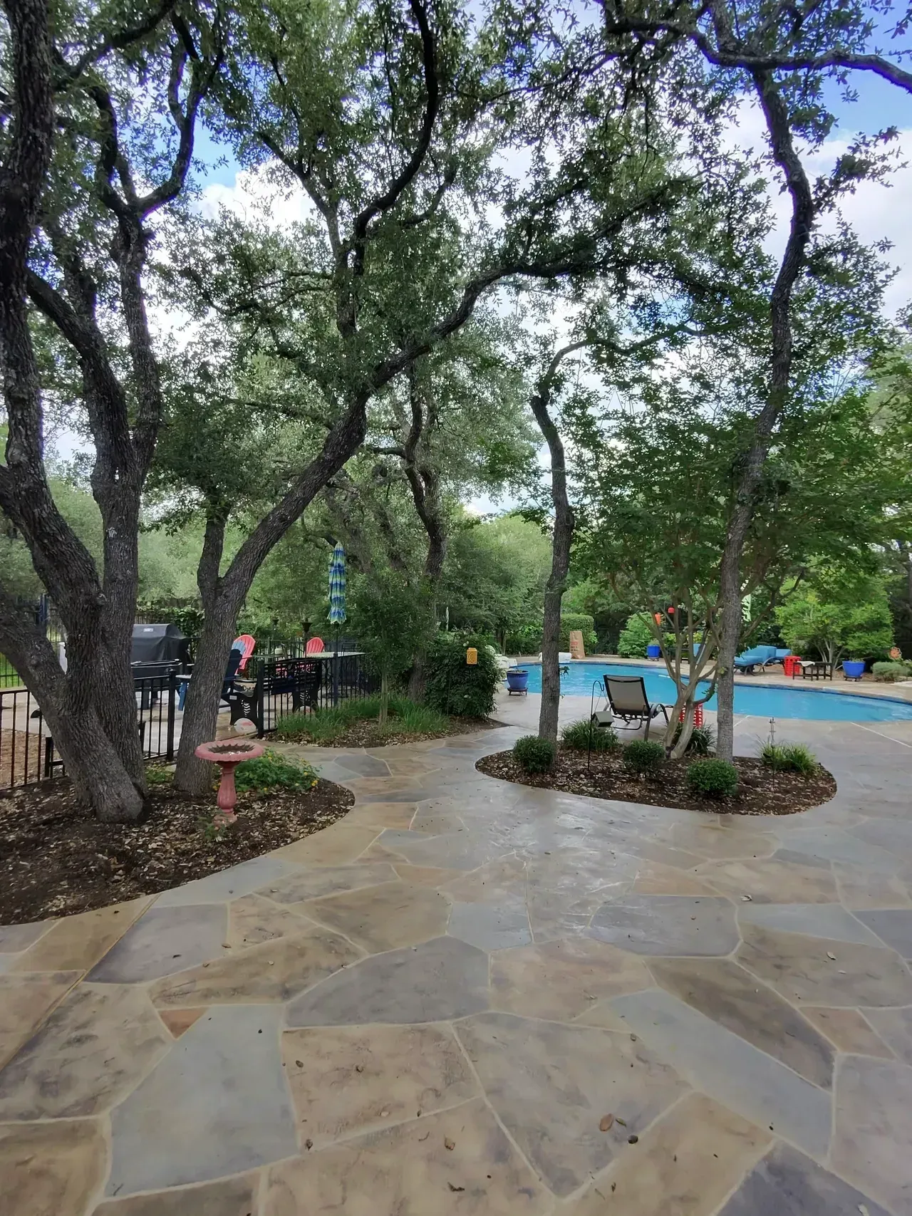 Flagstone patio with trees, a pool, and seating area in the background.