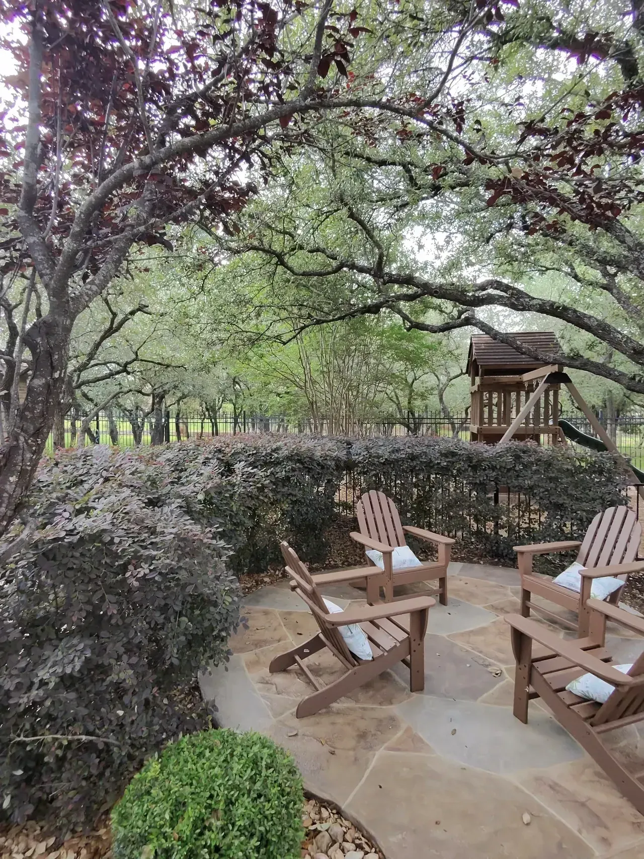 Patio with wooden chairs, surrounded by lush green trees and foliage.