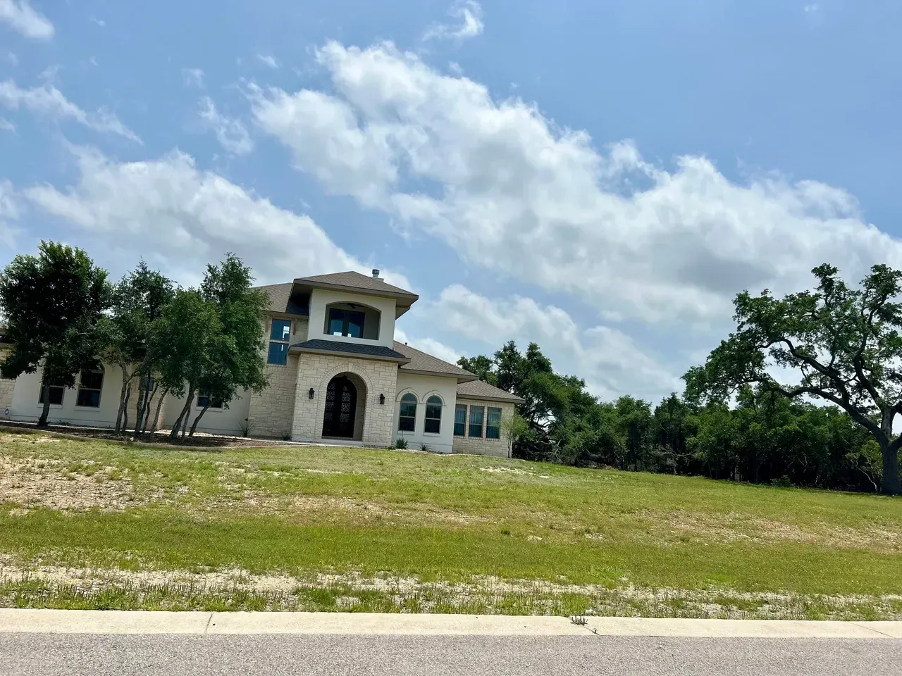 A light-colored house with a tiled roof sits on a grassy hill under a cloudy sky.