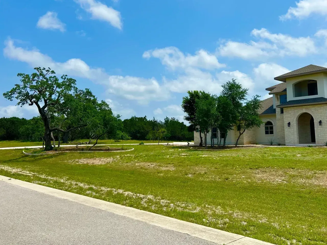 A large house with a stone facade sits next to a grassy lawn under a partly cloudy blue sky.