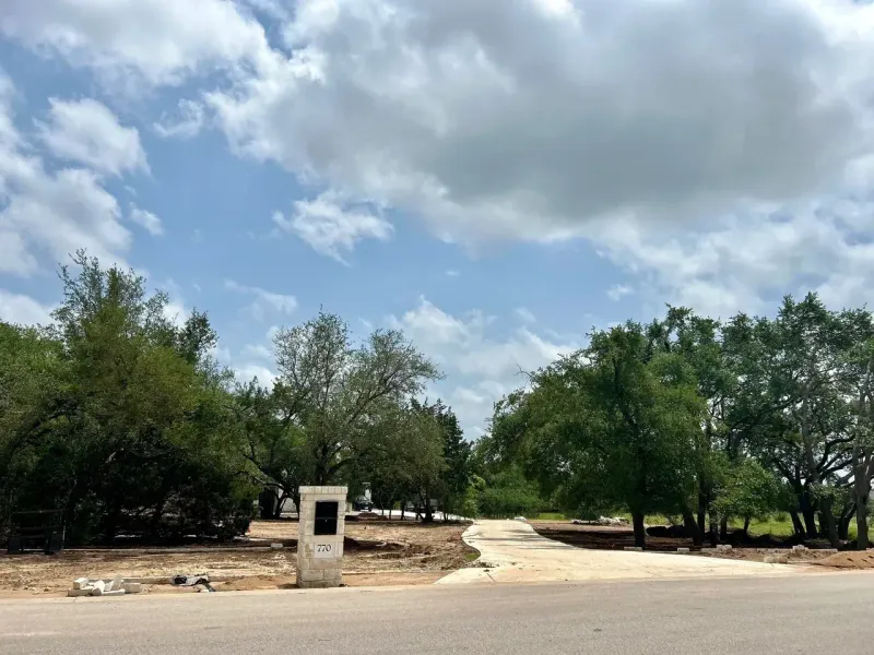 Paved road leads to a partially cleared area with trees and a cloudy sky. A white mailbox is present.