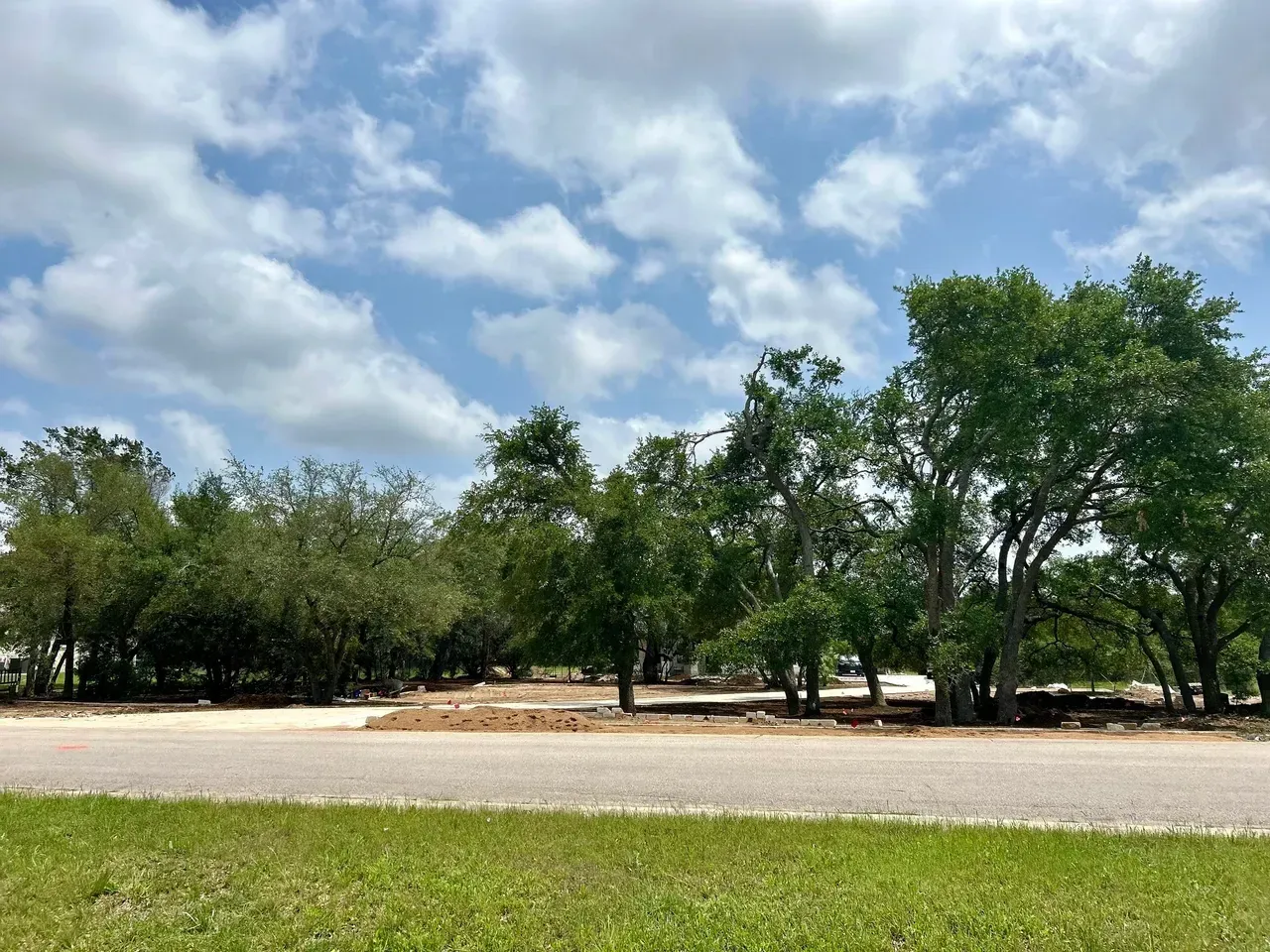 Paved road with trees and green grass under a partly cloudy blue sky.