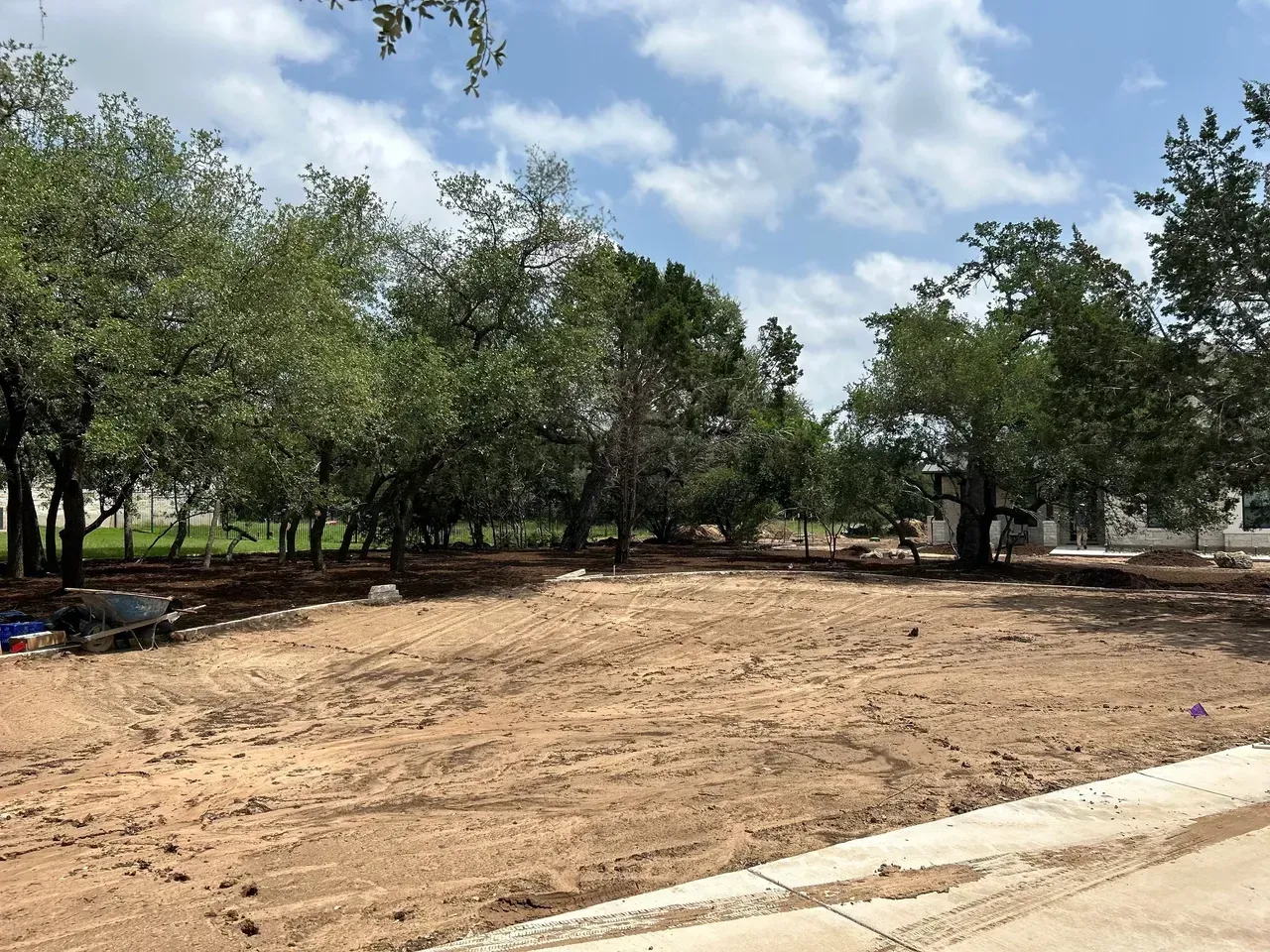 Cleared, dirt-covered lot in front of trees and a bright, cloudy sky.