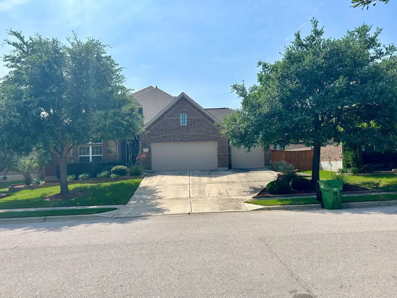 House with brick facade, two-car garage, and driveway. Two trees frame the front yard on a sunny day.