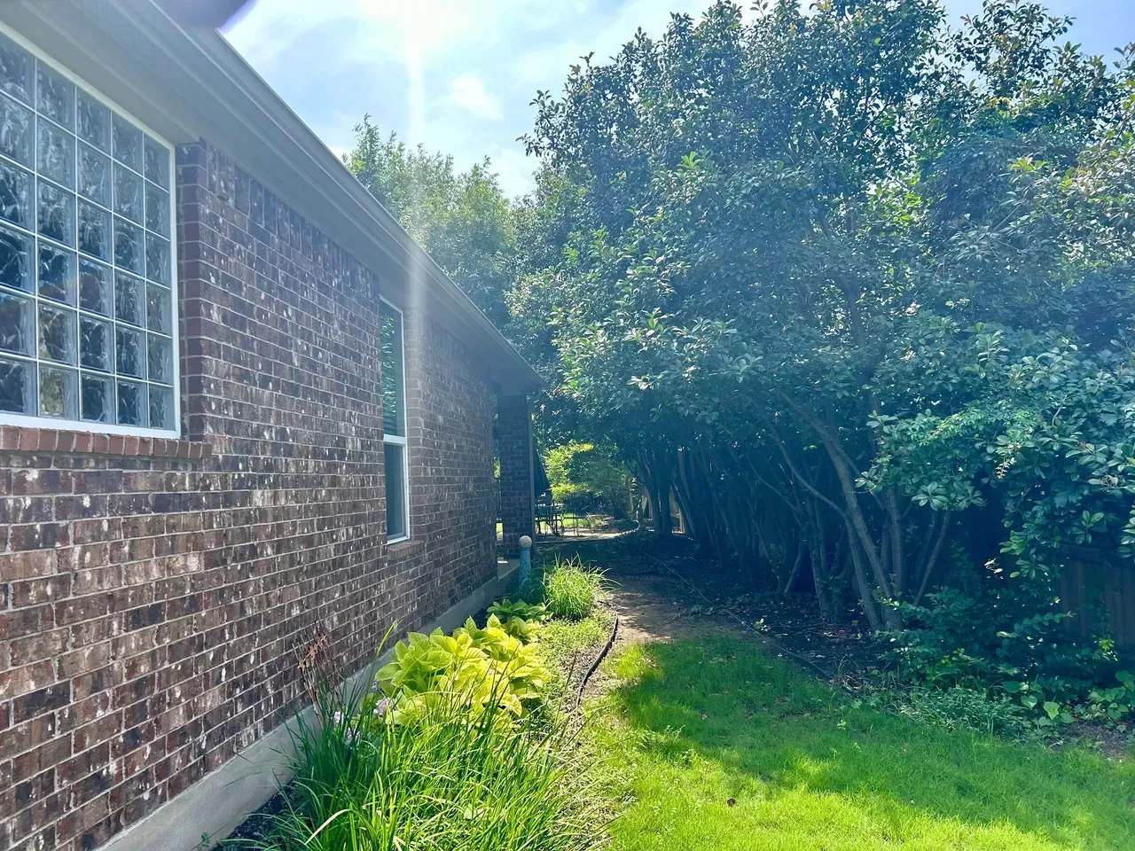 Brick building exterior next to a narrow grassy path with trees. Sunny day.