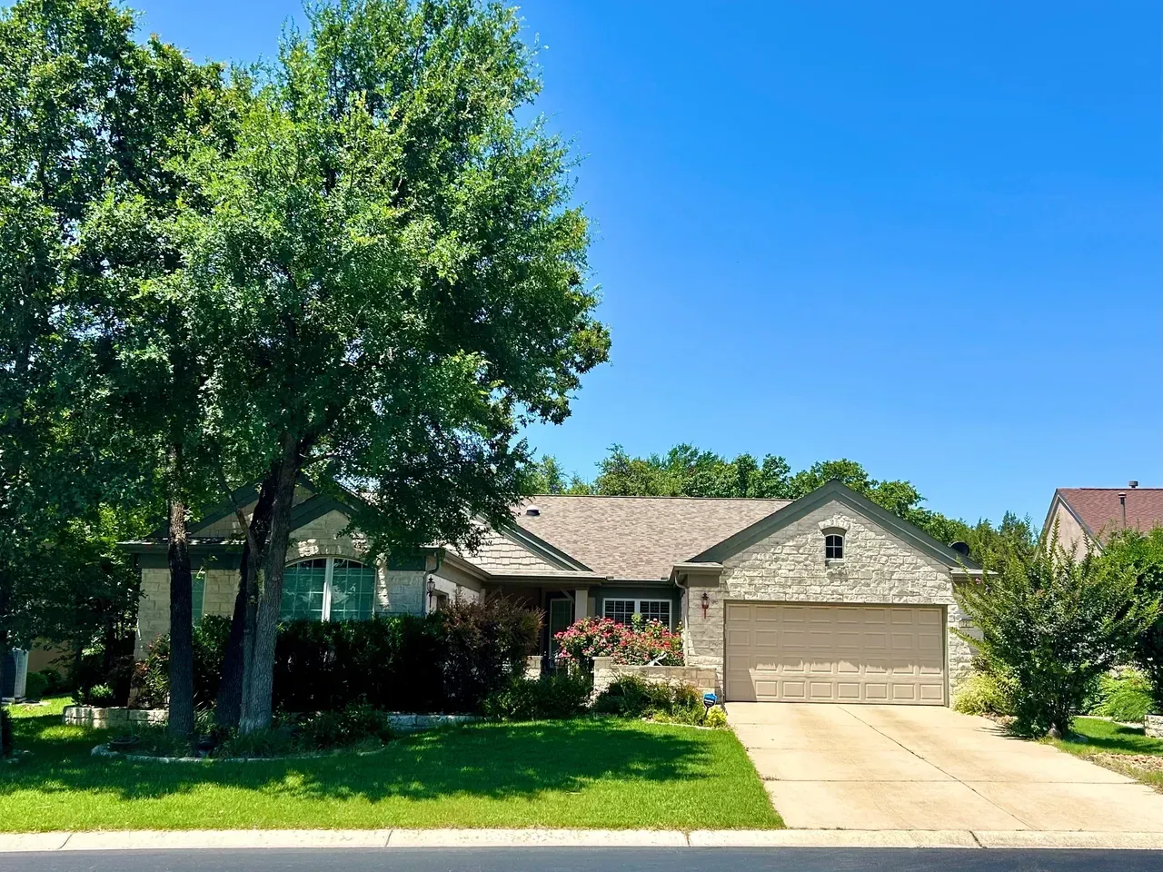 Tan brick house with a stone facade, beige garage door, and green lawn under a blue sky.