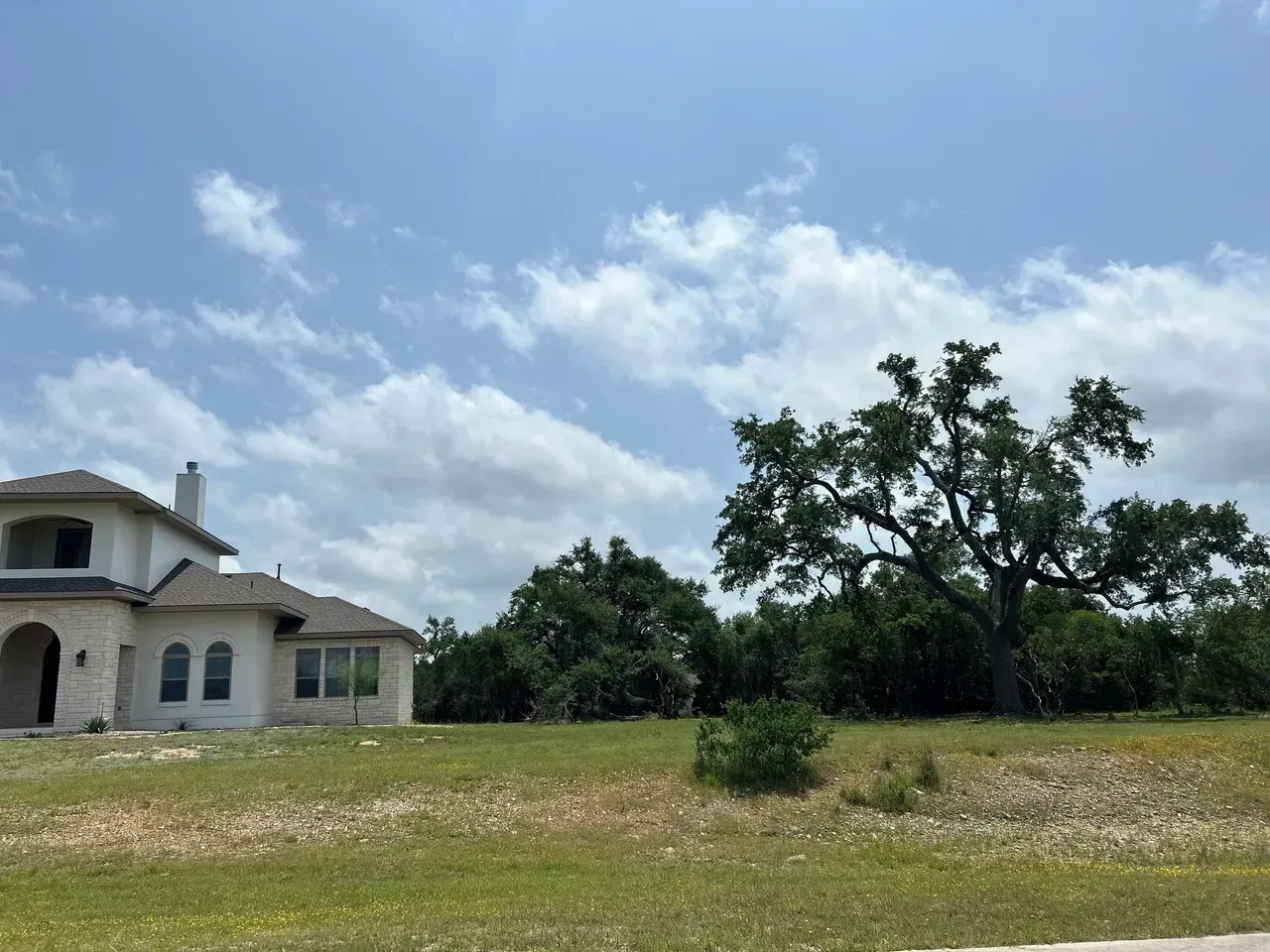 House on a grassy hill with trees under a cloudy sky.