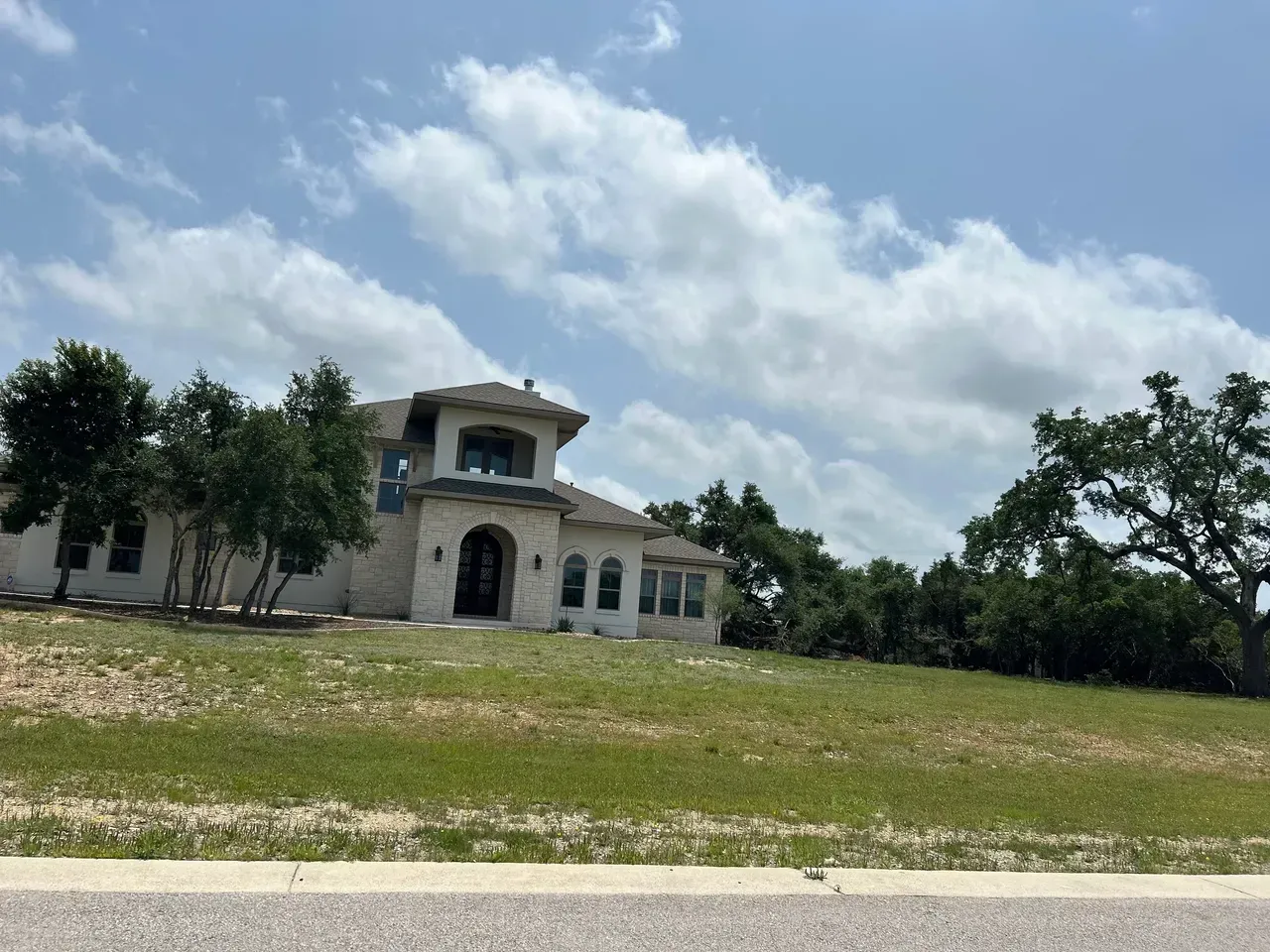 Large, white house on a grassy hill under a partly cloudy sky.