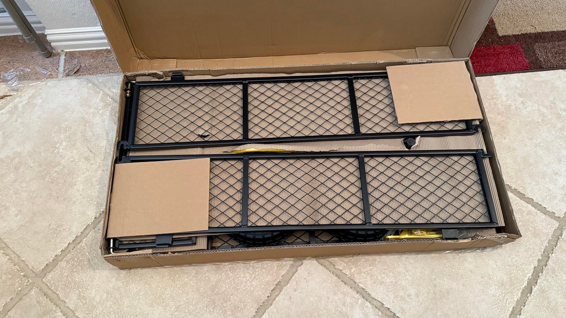 Open cardboard box containing black metal mesh shelves and cardboard packing material.