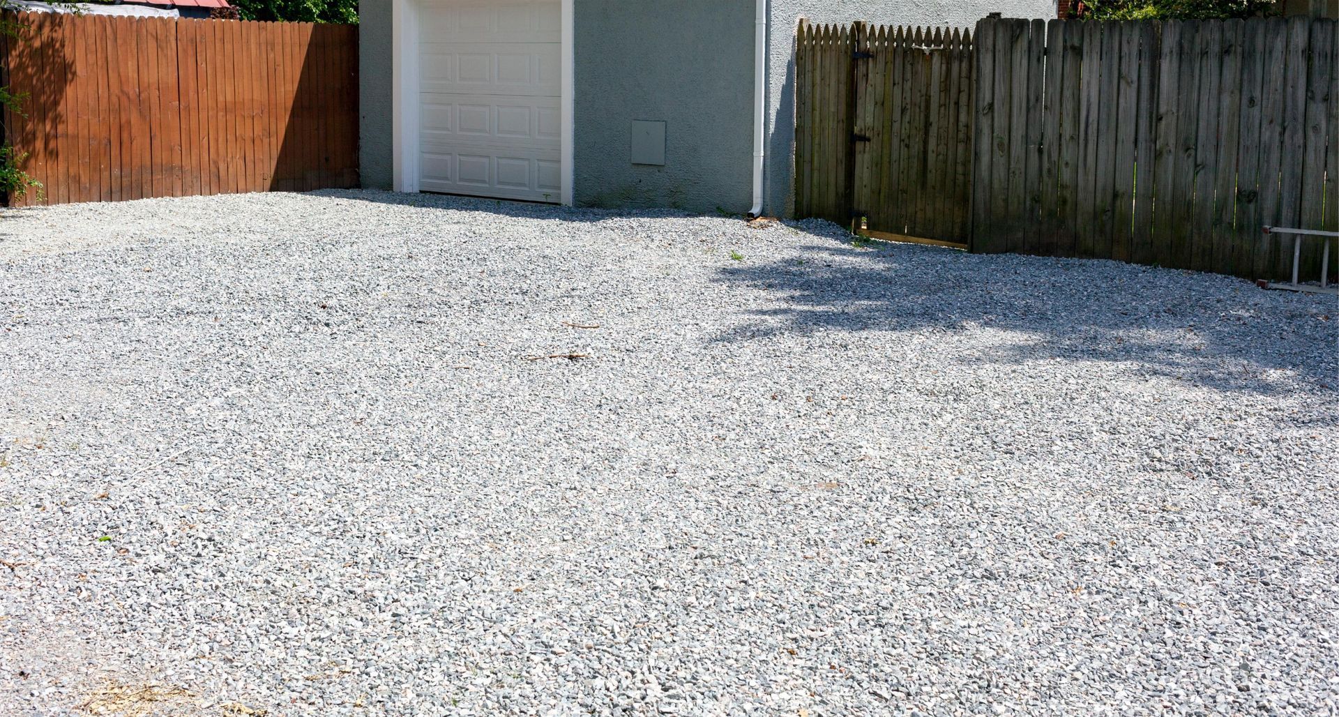 A light-colored gravel driveway leads up to a white garage door, flanked by wooden fences.