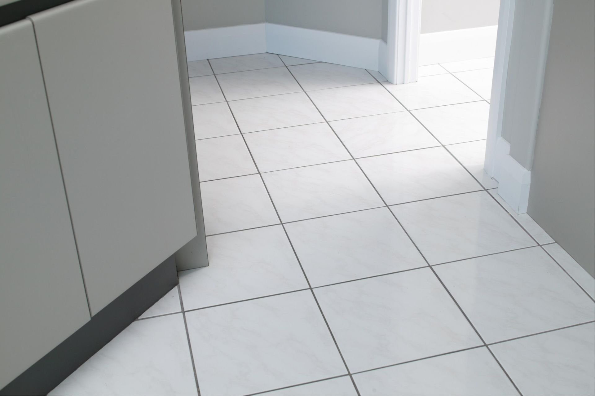White square floor tiles in a home interior, leading towards a doorway with white baseboards and grey walls.