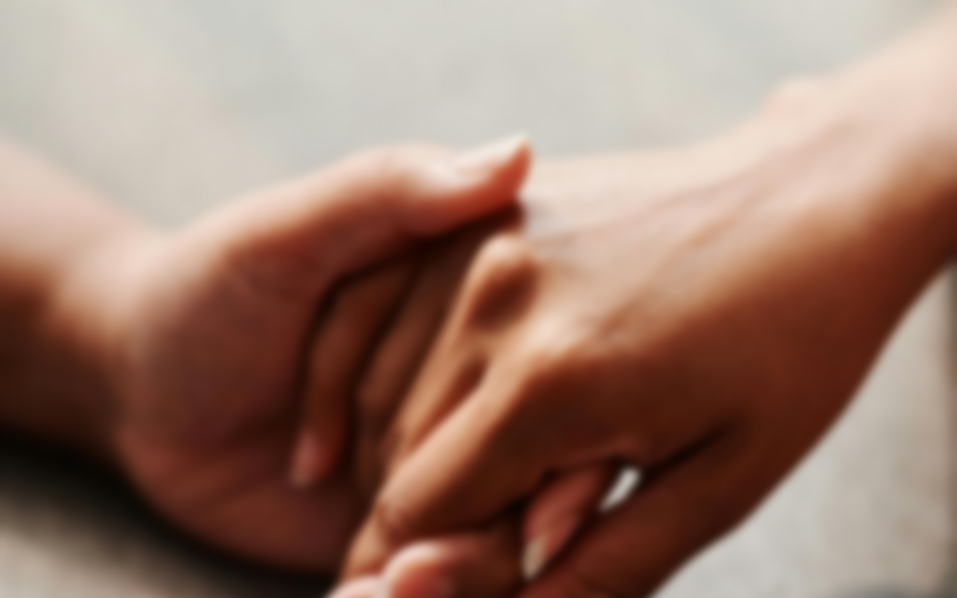 Two hands gently clasped together on a soft gray surface.