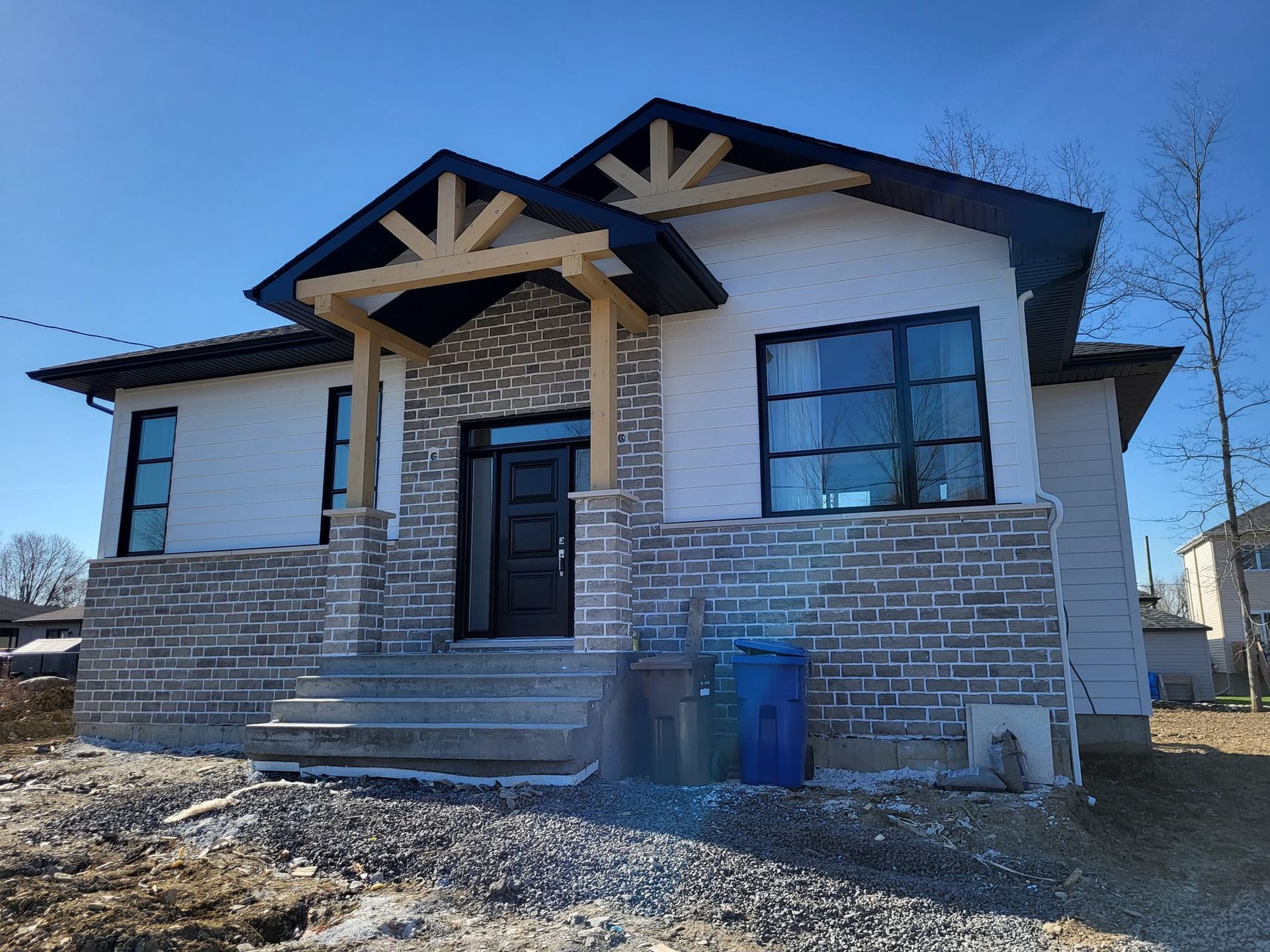 Une maison en briques blanches avec un toit noir est en construction.