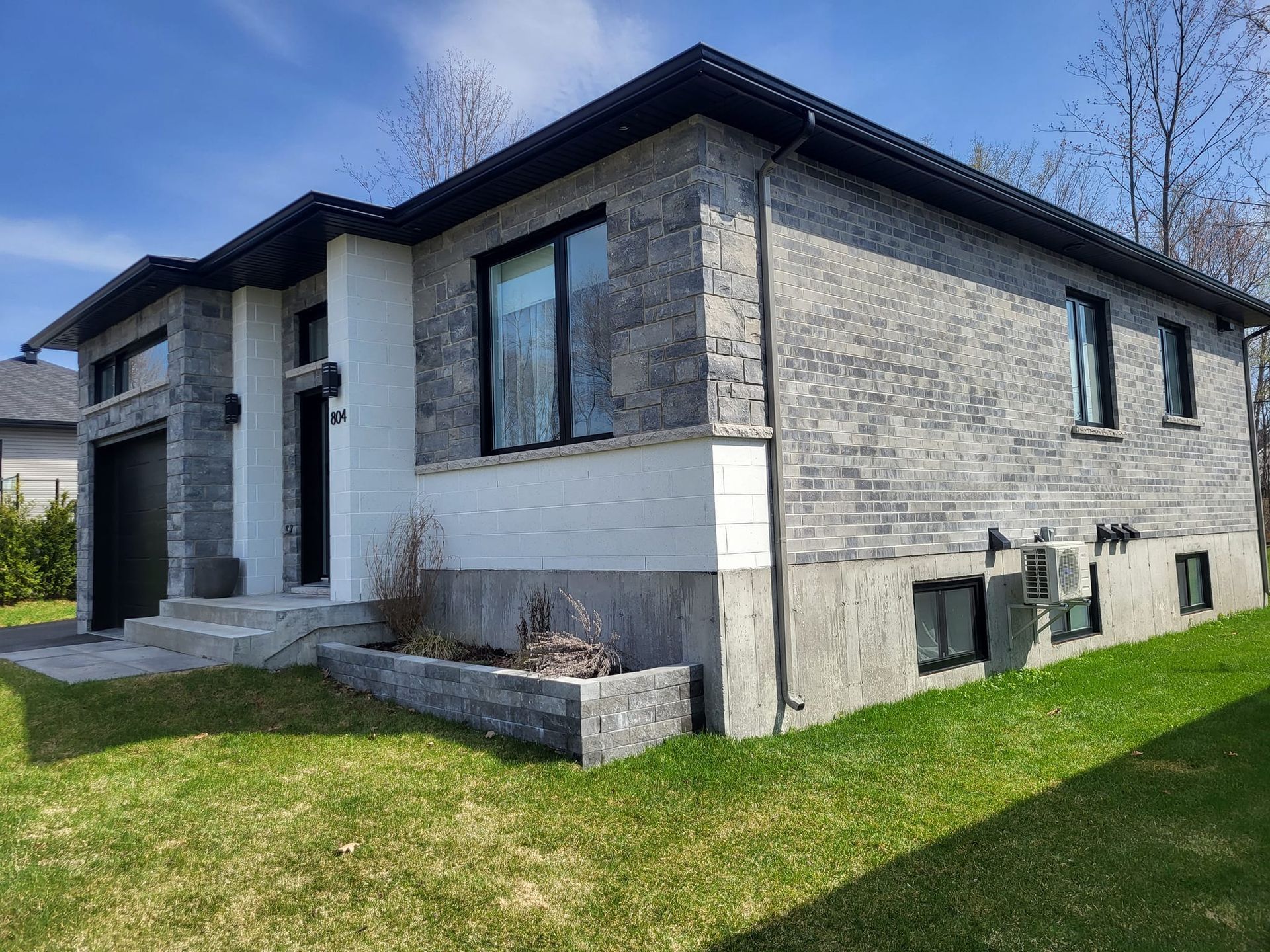 Une petite maison en briques avec beaucoup de fenêtres est située au sommet d'une pelouse verte luxuriante.