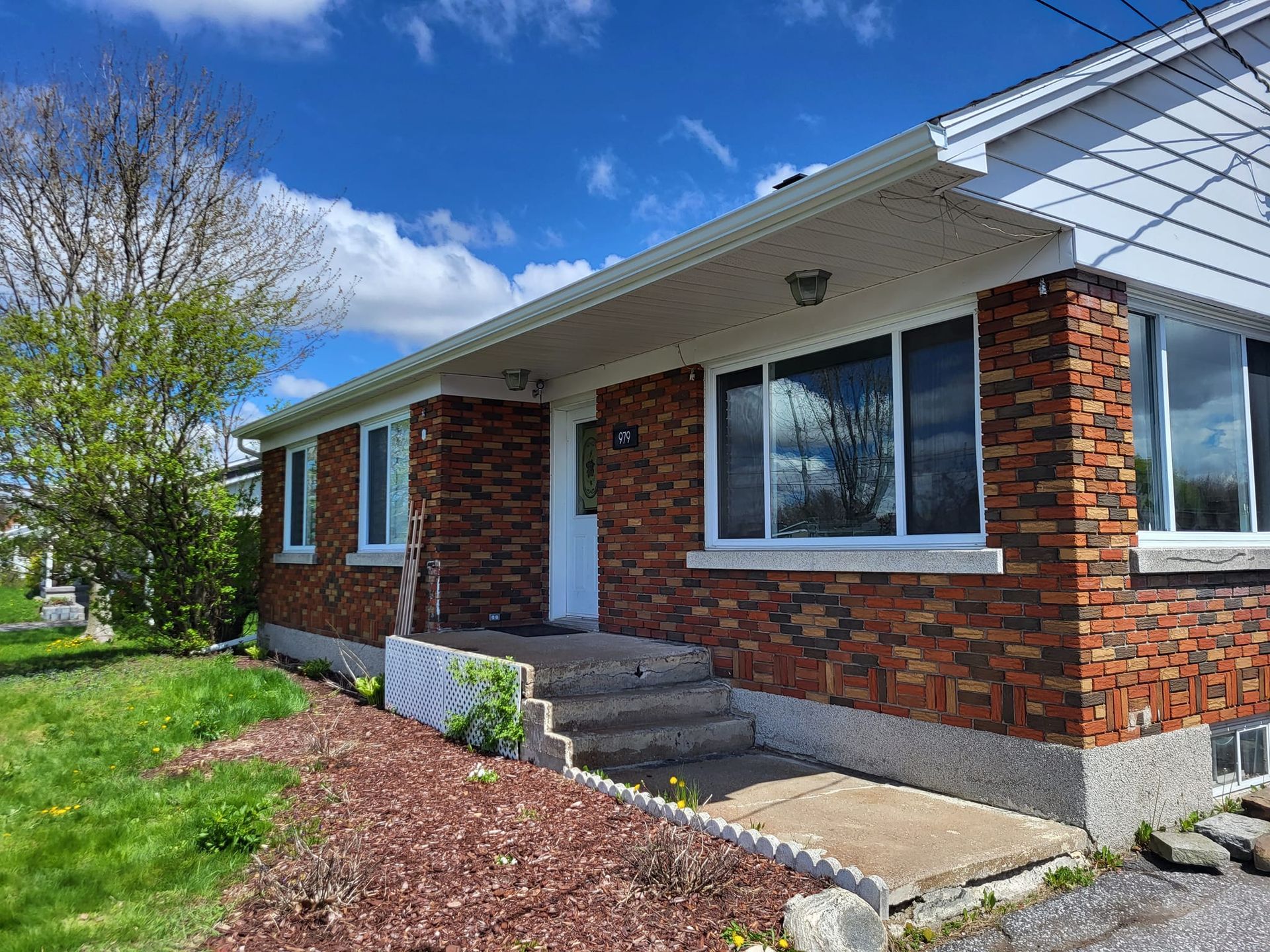 Une maison en briques avec un toit blanc et beaucoup de fenêtres par une journée ensoleillée.