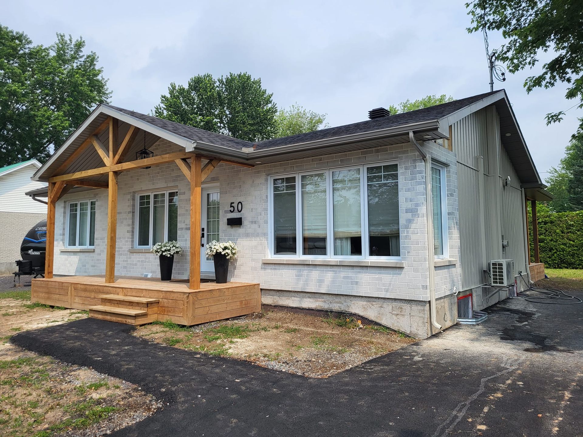 Une petite maison blanche avec un porche en bois et une voiture garée devant.