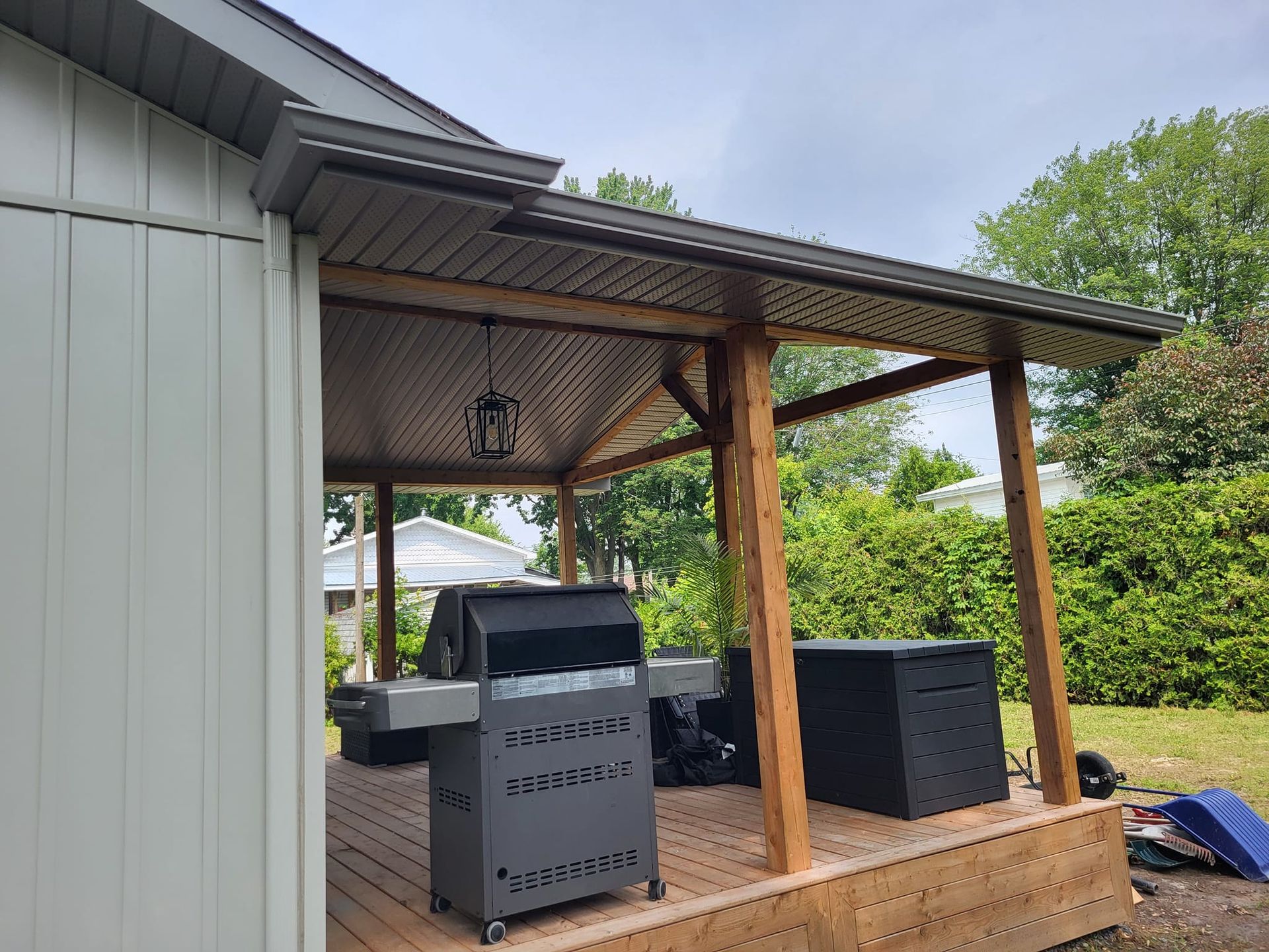 Un gril est posé sur une terrasse en bois sous un porche couvert.