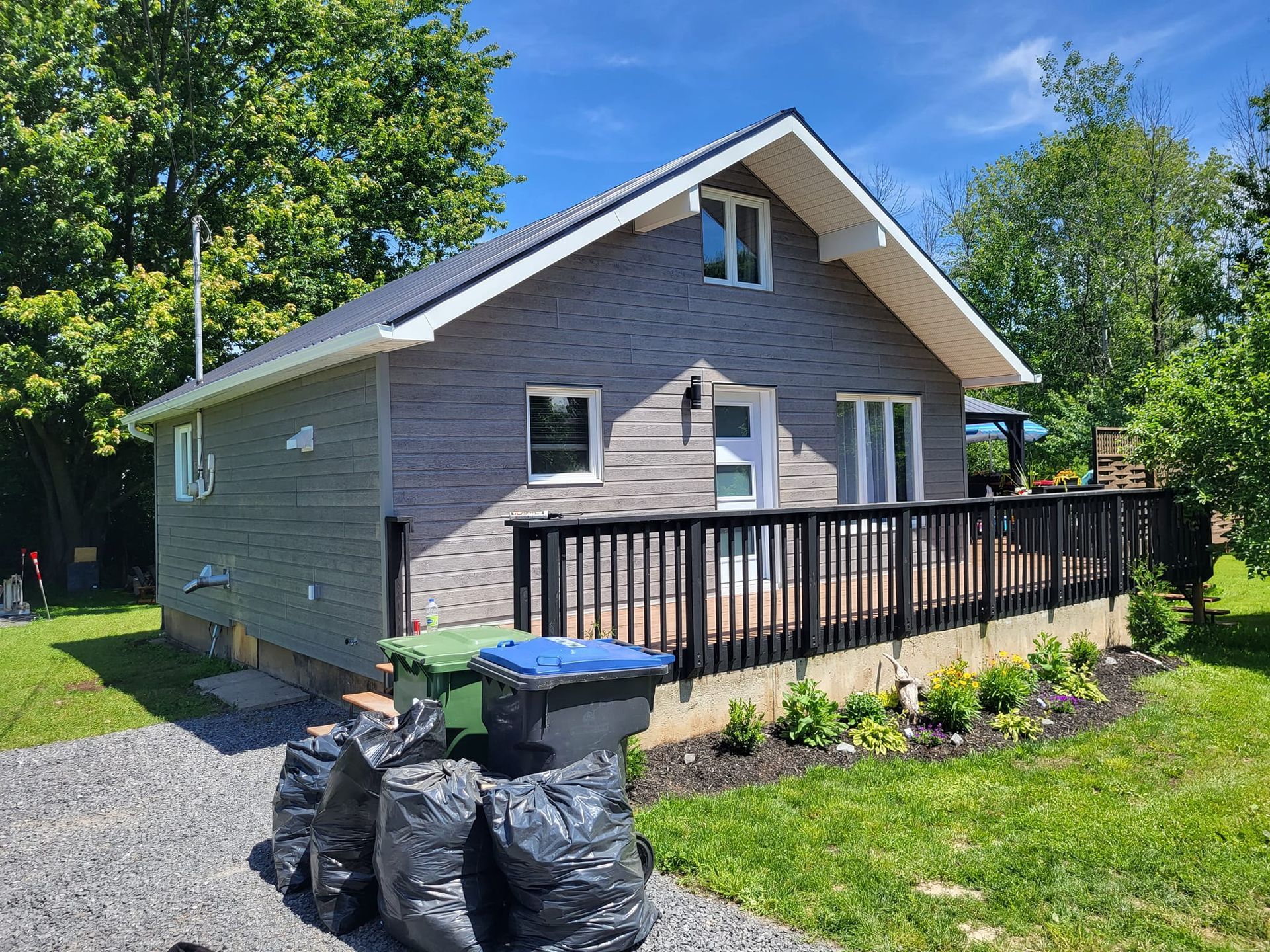 Une petite maison avec une terrasse et des poubelles devant.