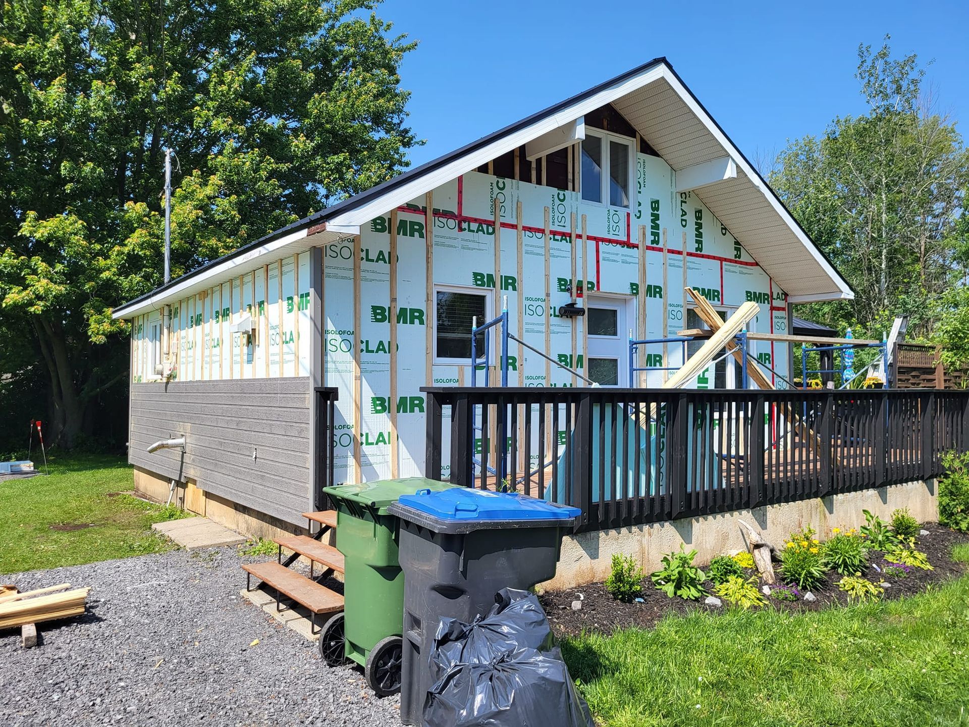 Une maison est en construction avec une terrasse et une poubelle devant.