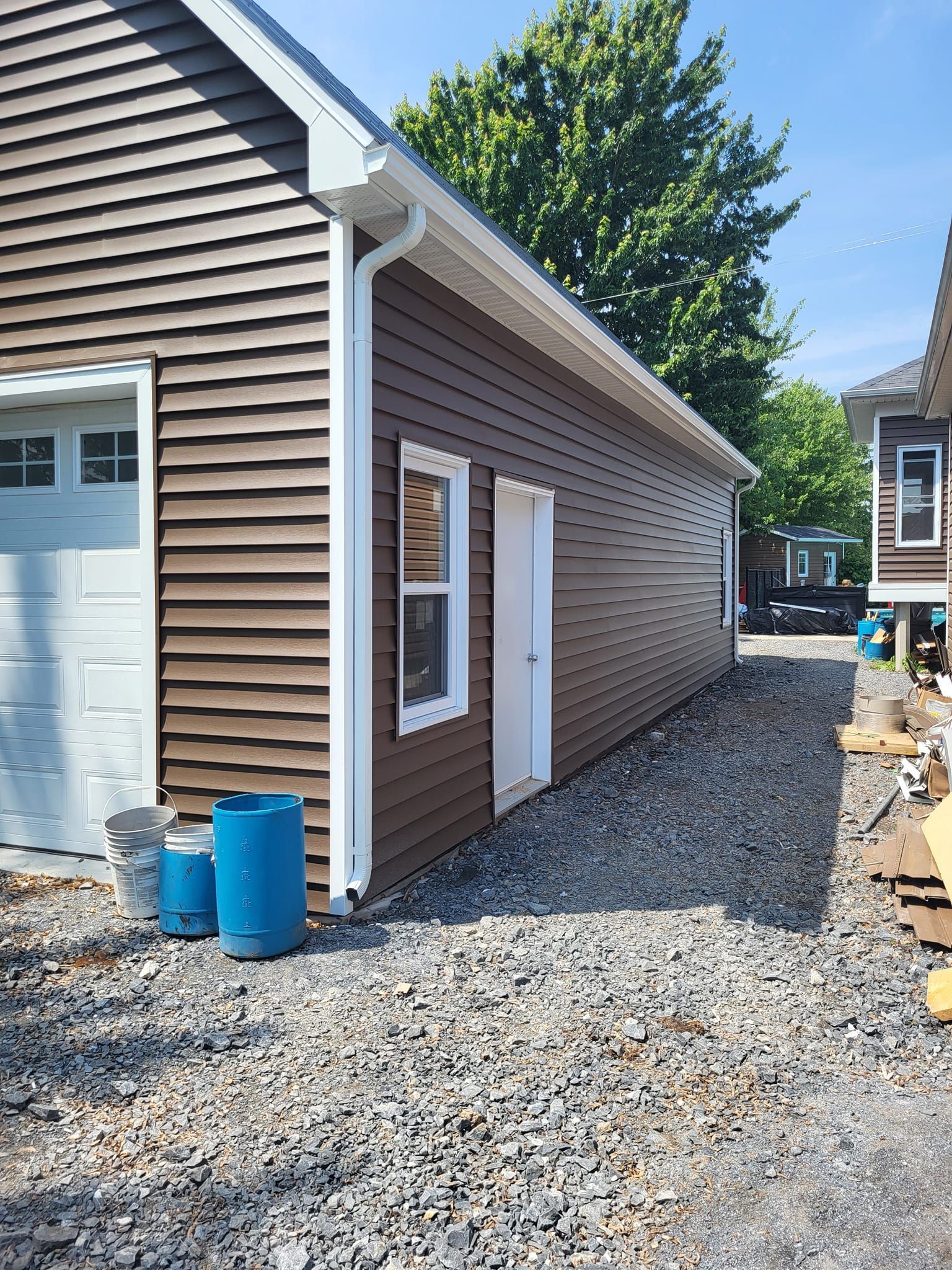 Une maison brune avec une porte de garage blanche et un tonneau bleu devant.