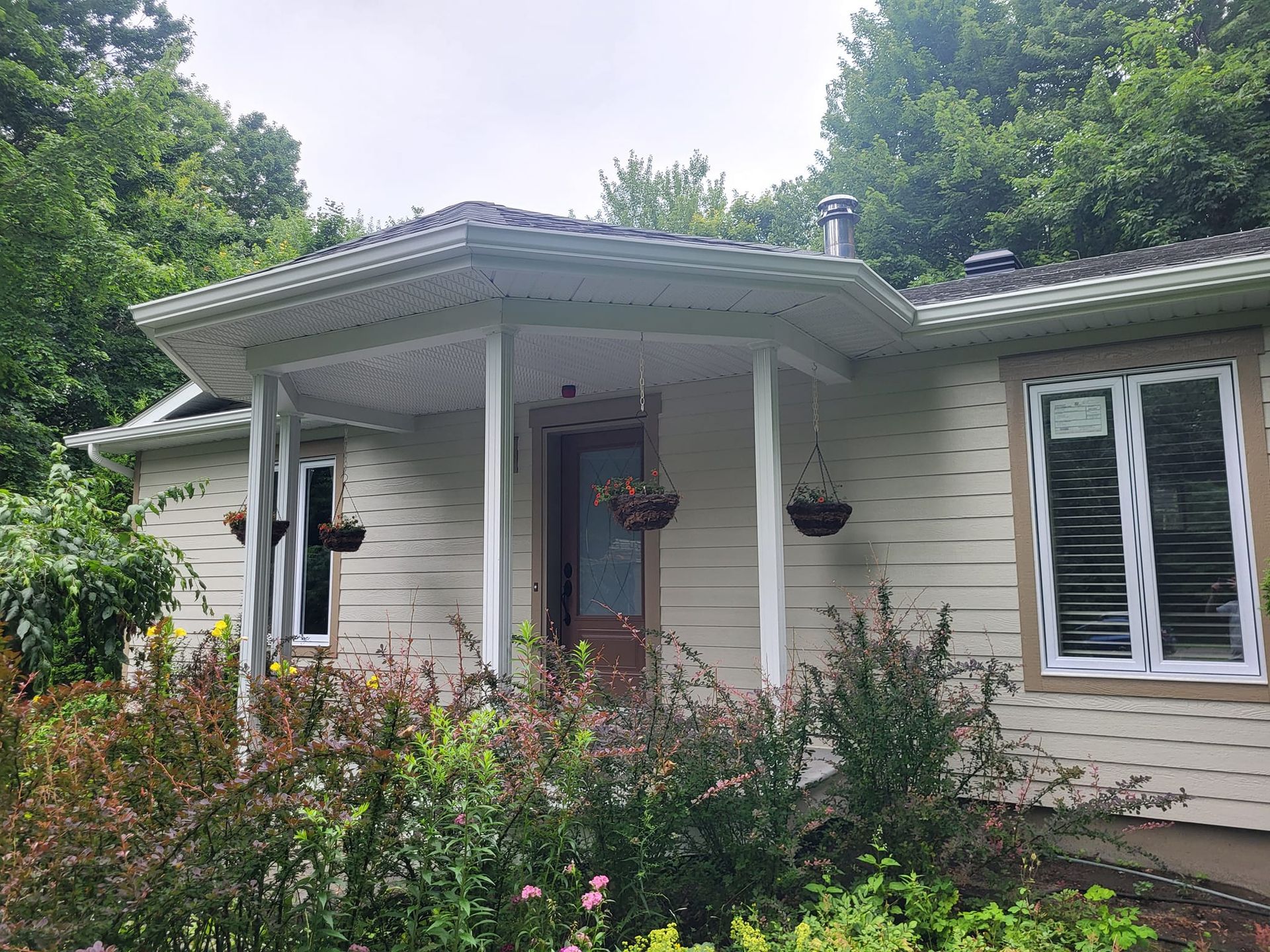 Une maison blanche avec un porche entouré d'arbres et de buissons.