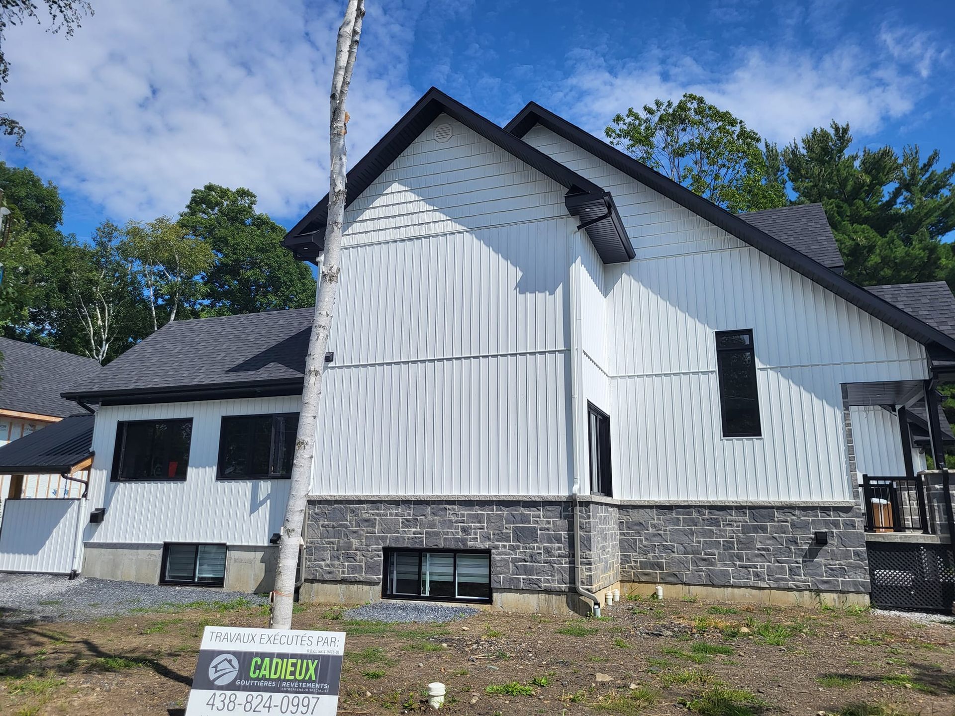 Une maison blanche avec un toit noir et un panneau devant.