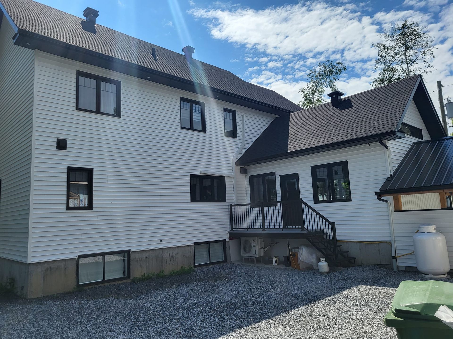 Une grande maison blanche avec un toit noir est posée sur un terrain en gravier.