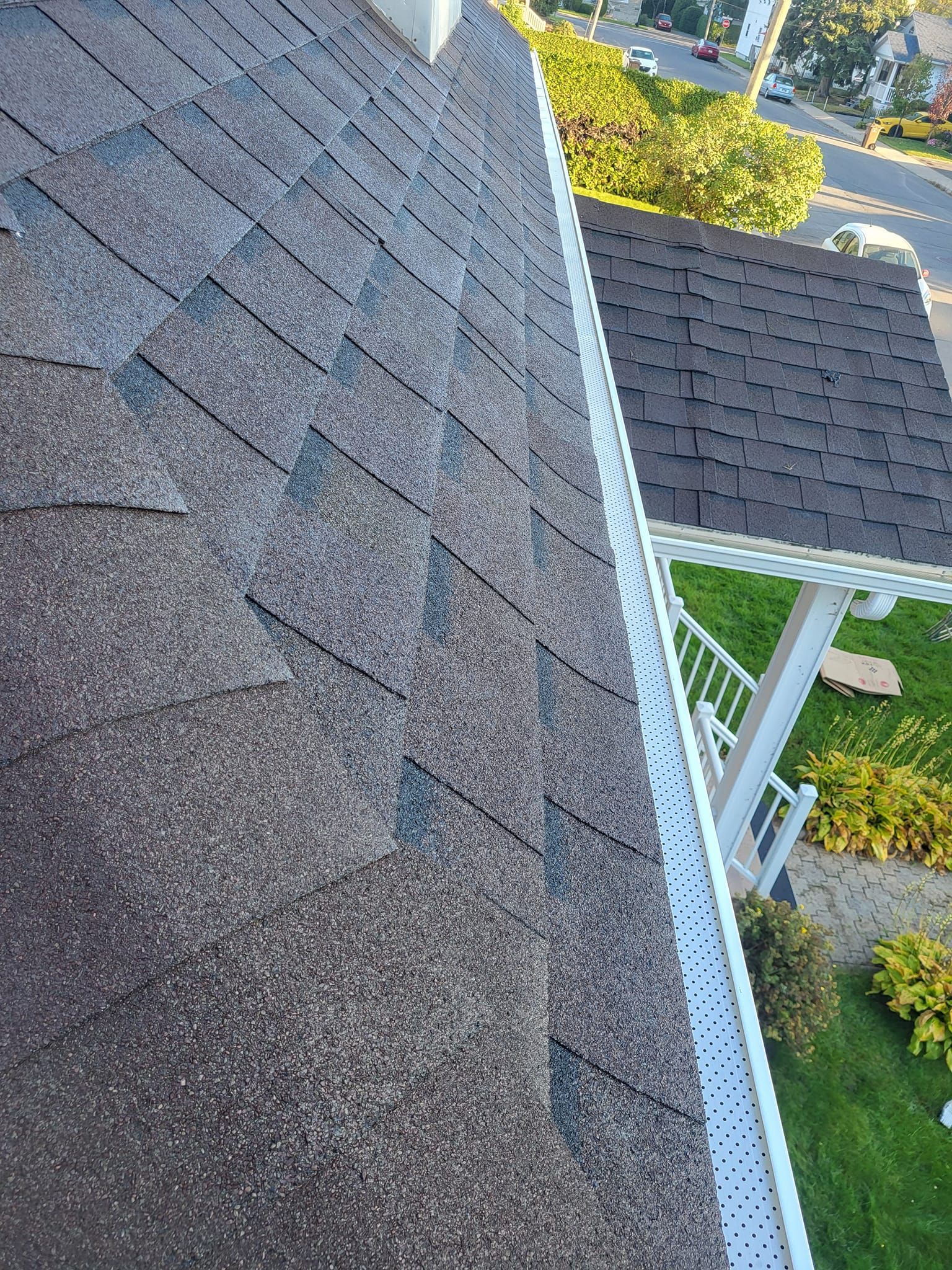 Un gros plan d'un toit avec une gouttière blanche et une maison en arrière-plan.