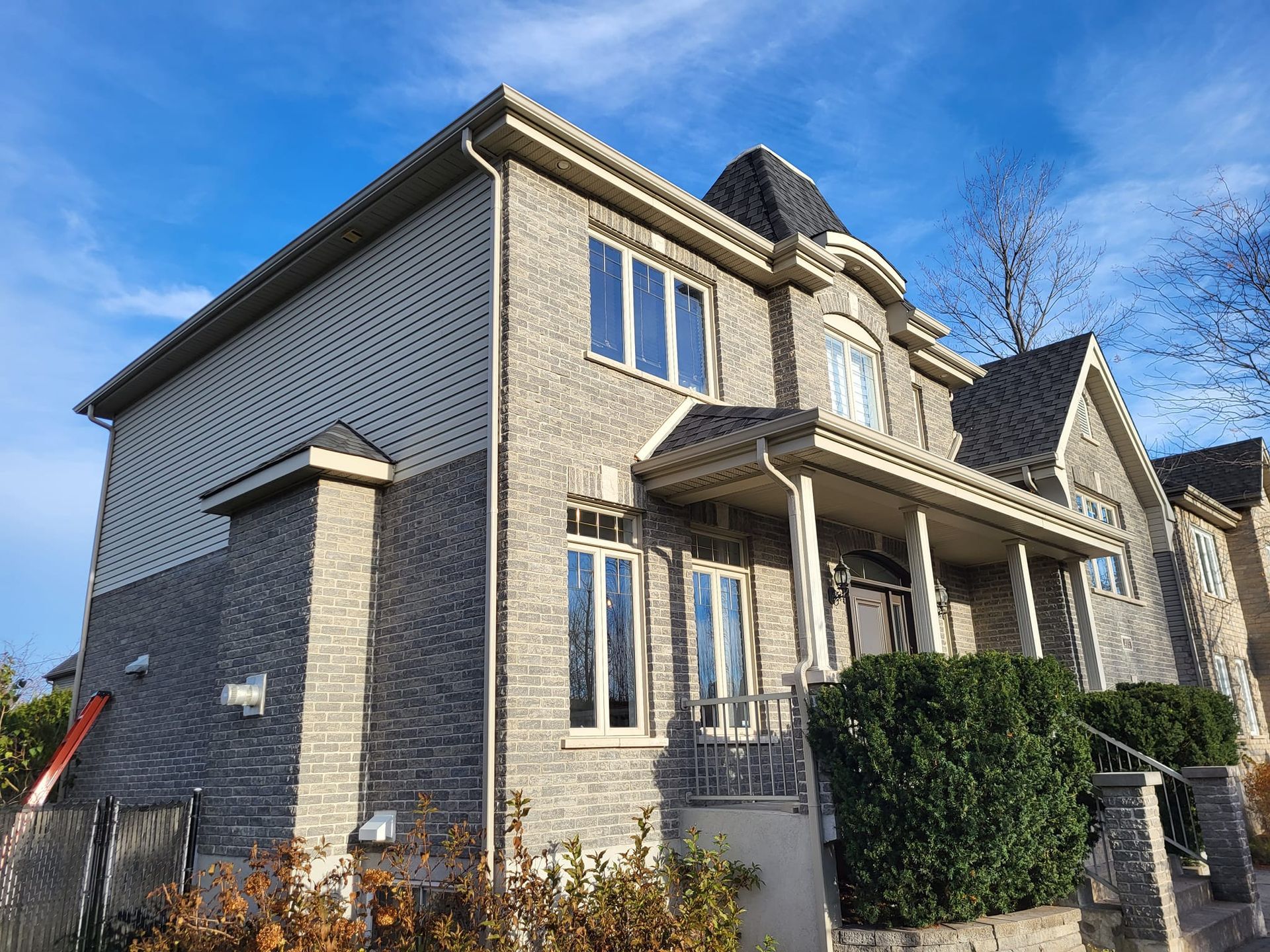 Une grande maison en briques avec un porche et un ciel bleu en arrière-plan.