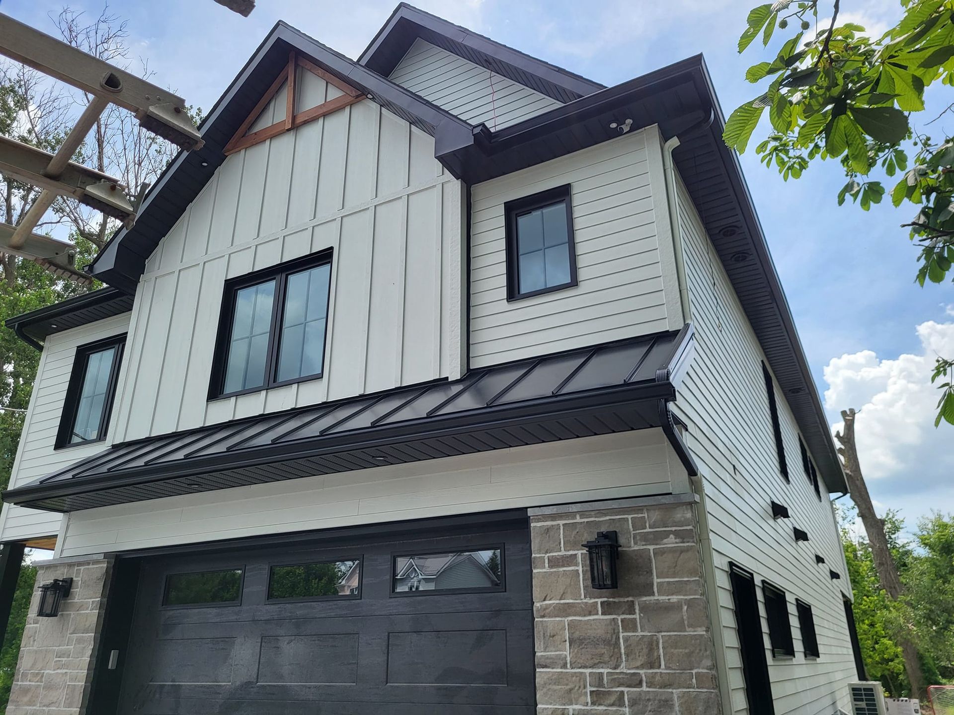 Une maison blanche avec une porte de garage noire et un toit noir.