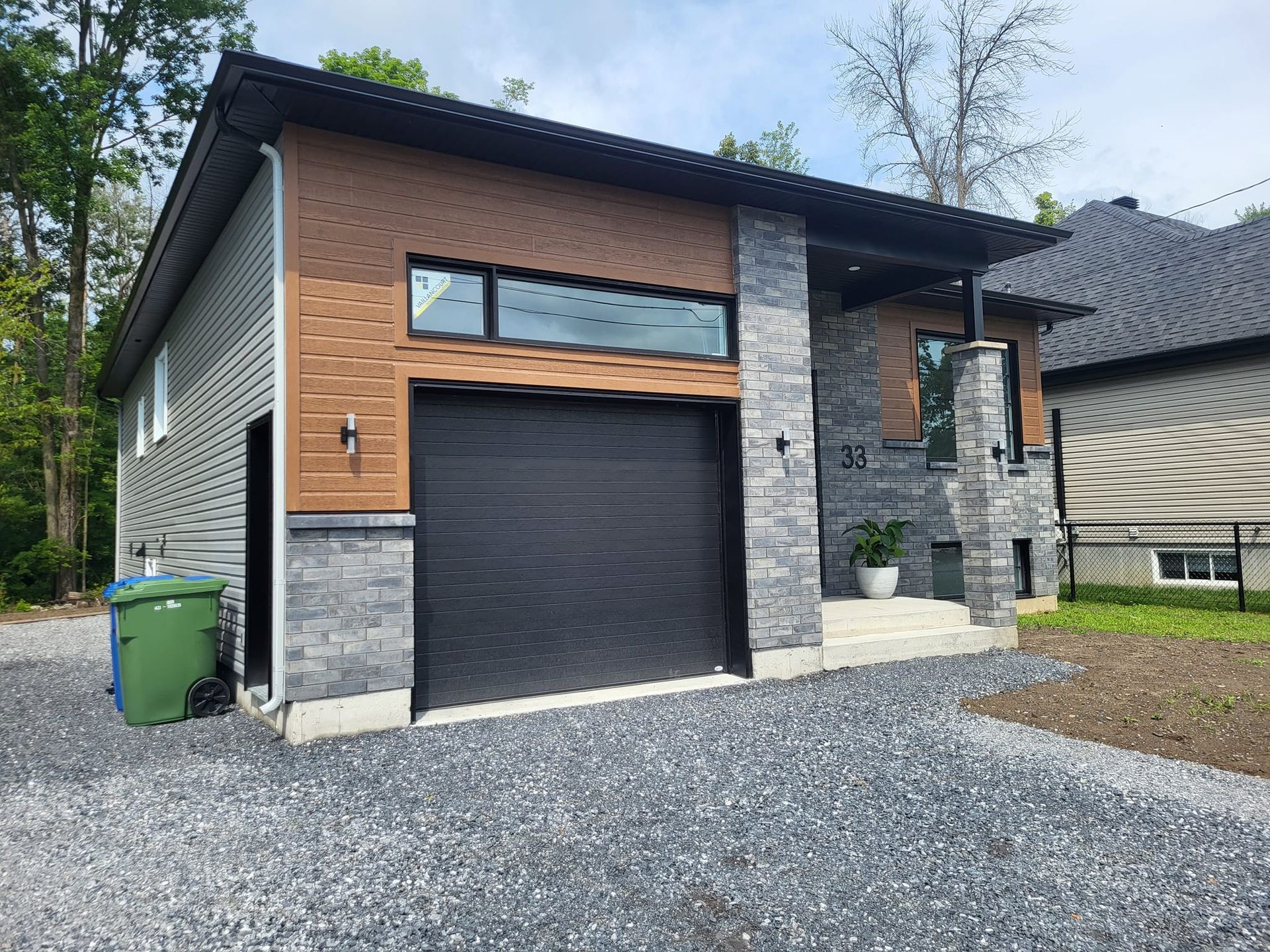 Une maison avec un garage et une poubelle verte devant.