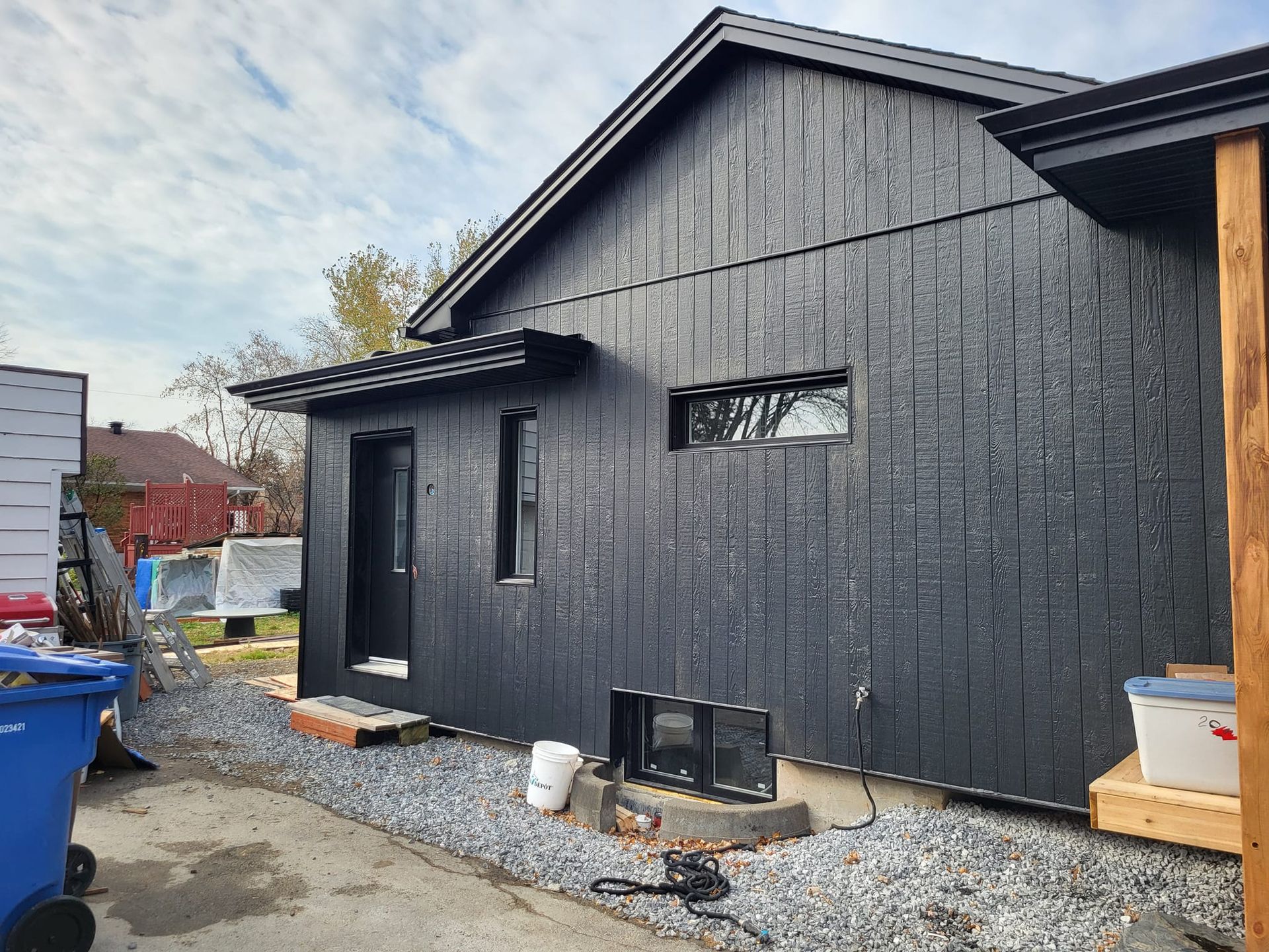 Une maison noire avec une poubelle bleue devant.