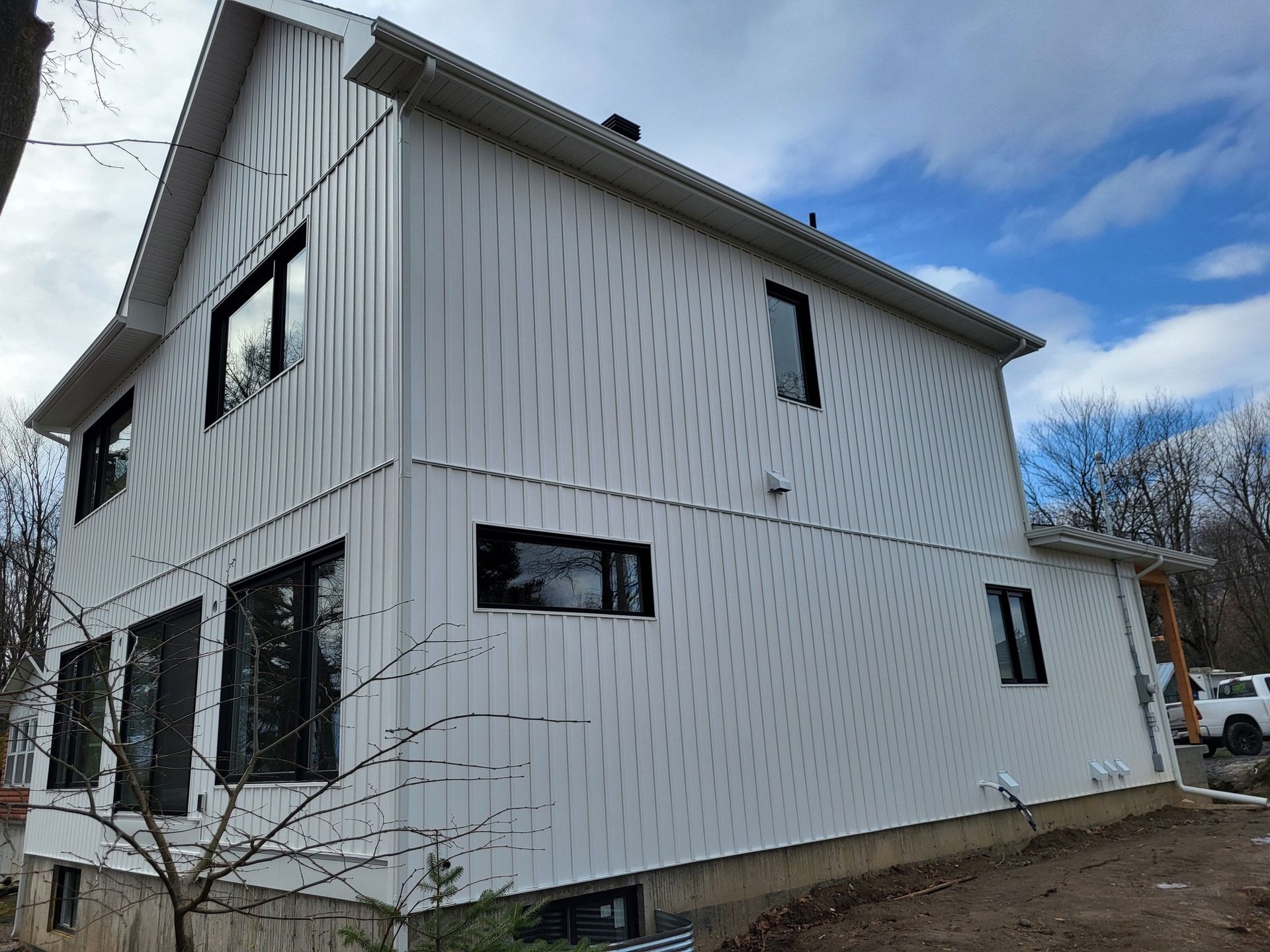 Une maison blanche avec des fenêtres noires et un ciel bleu en arrière-plan.