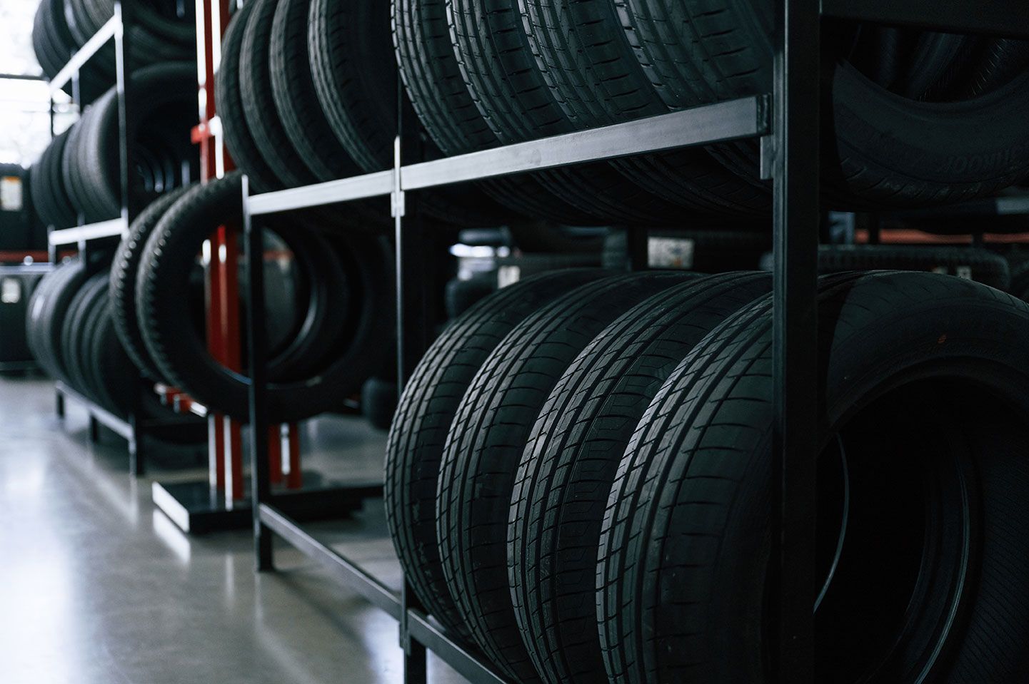 Tires stacked on black metal shelves in a garage or warehouse, with a concrete floor.