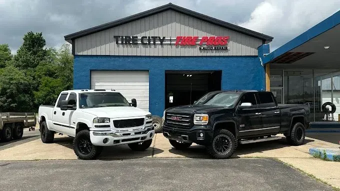 Two pickup trucks parked in front of a blue Tire City auto shop.