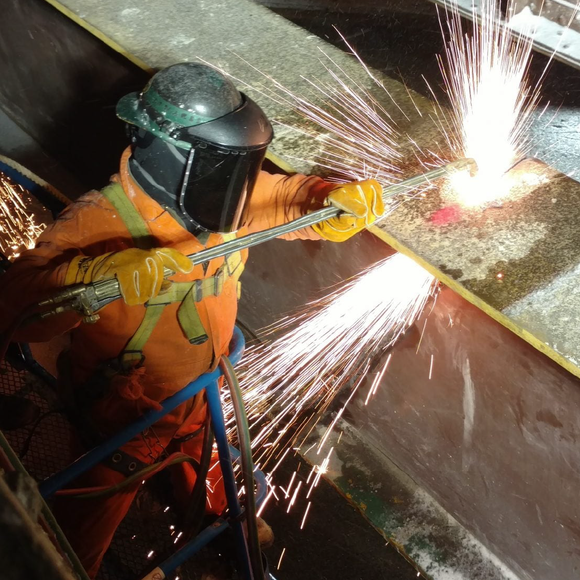 A man wearing a helmet and gloves is welding a piece of metal