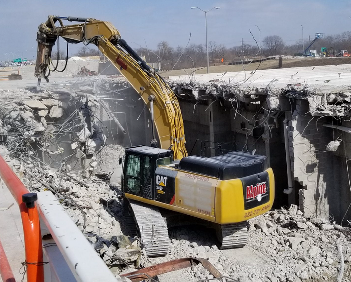 A large yellow excavator is demolishing a bridge.